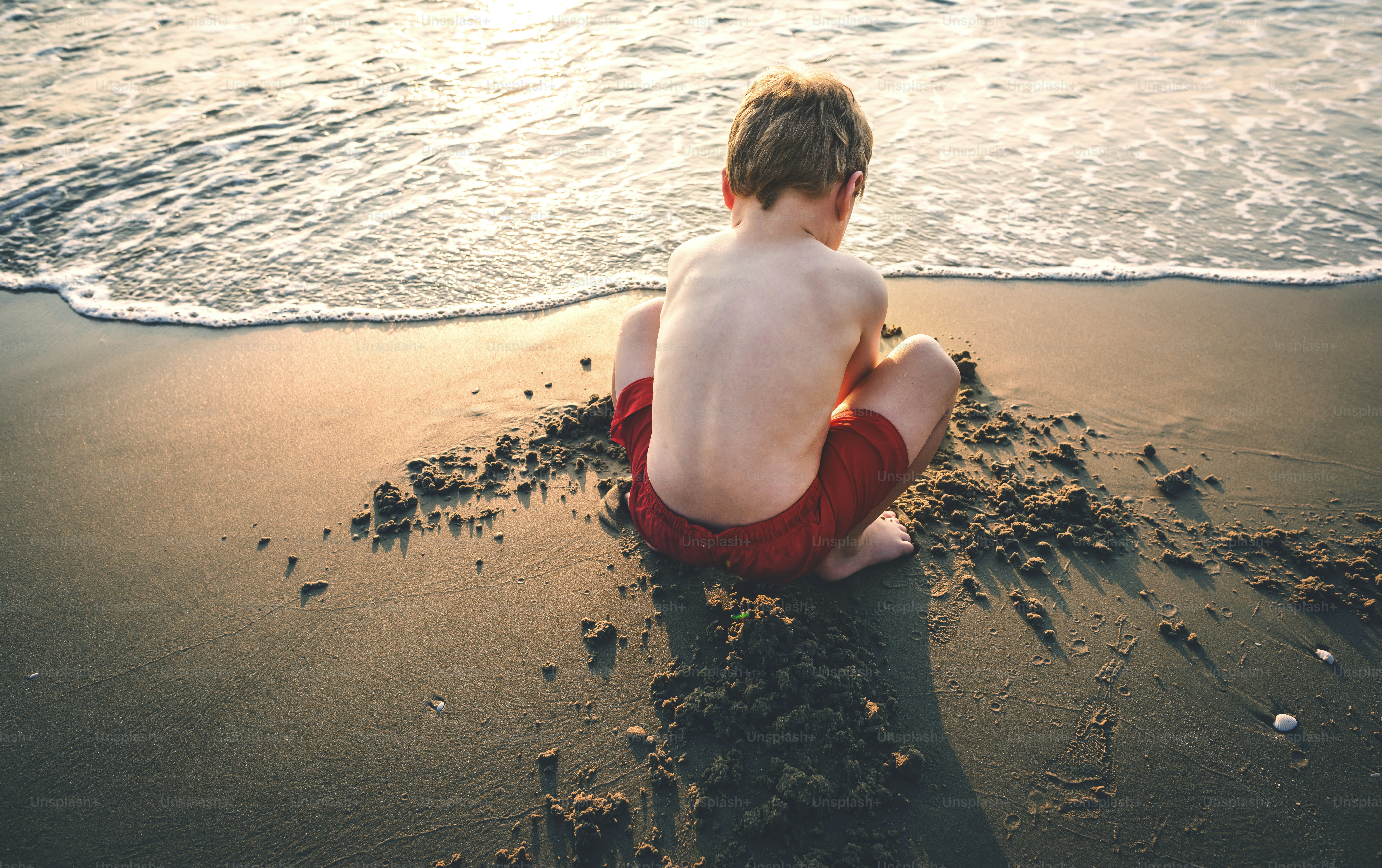child building sandcastle on a beach at sunset with waves nearby