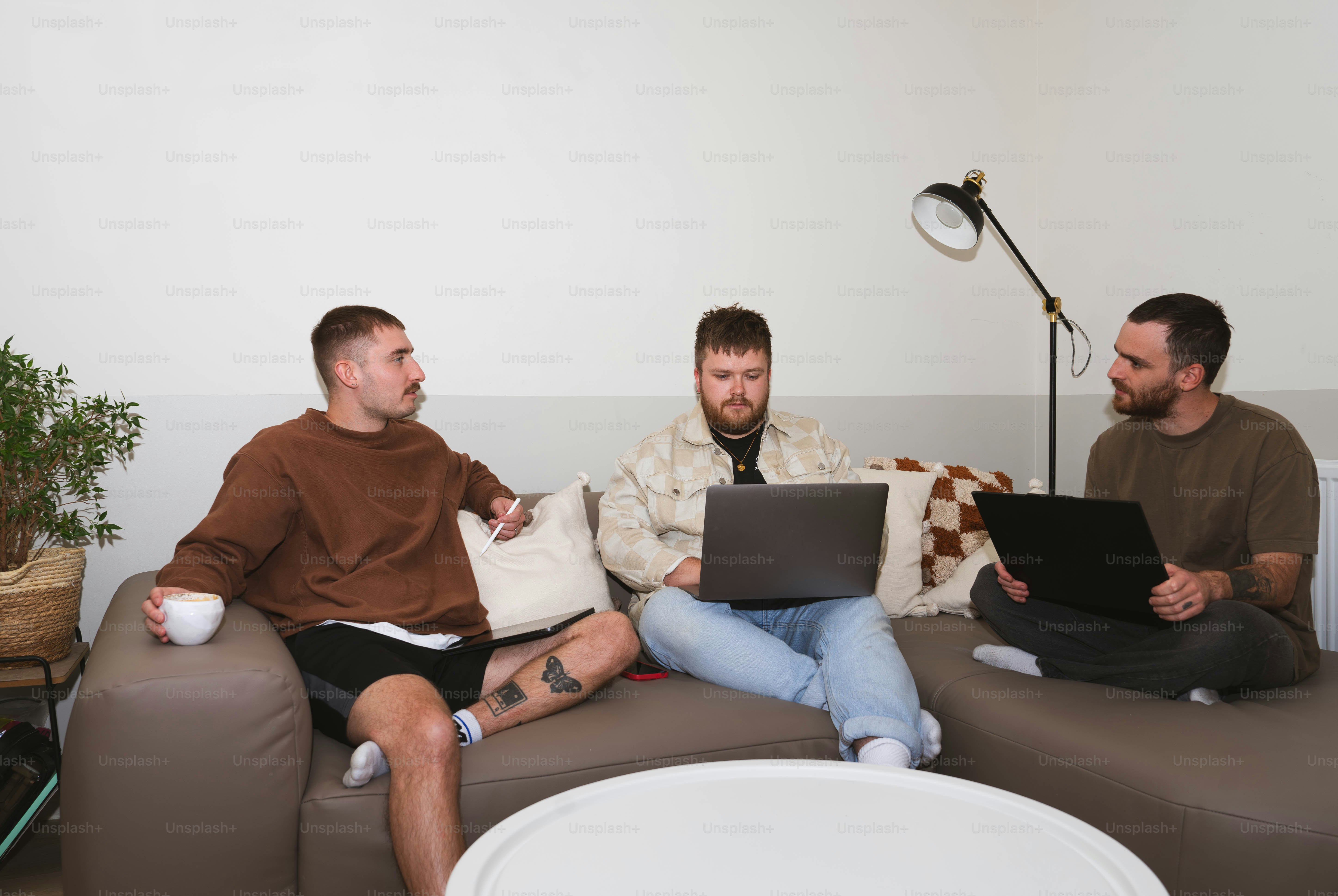 Three men sitting on a couch with laptops