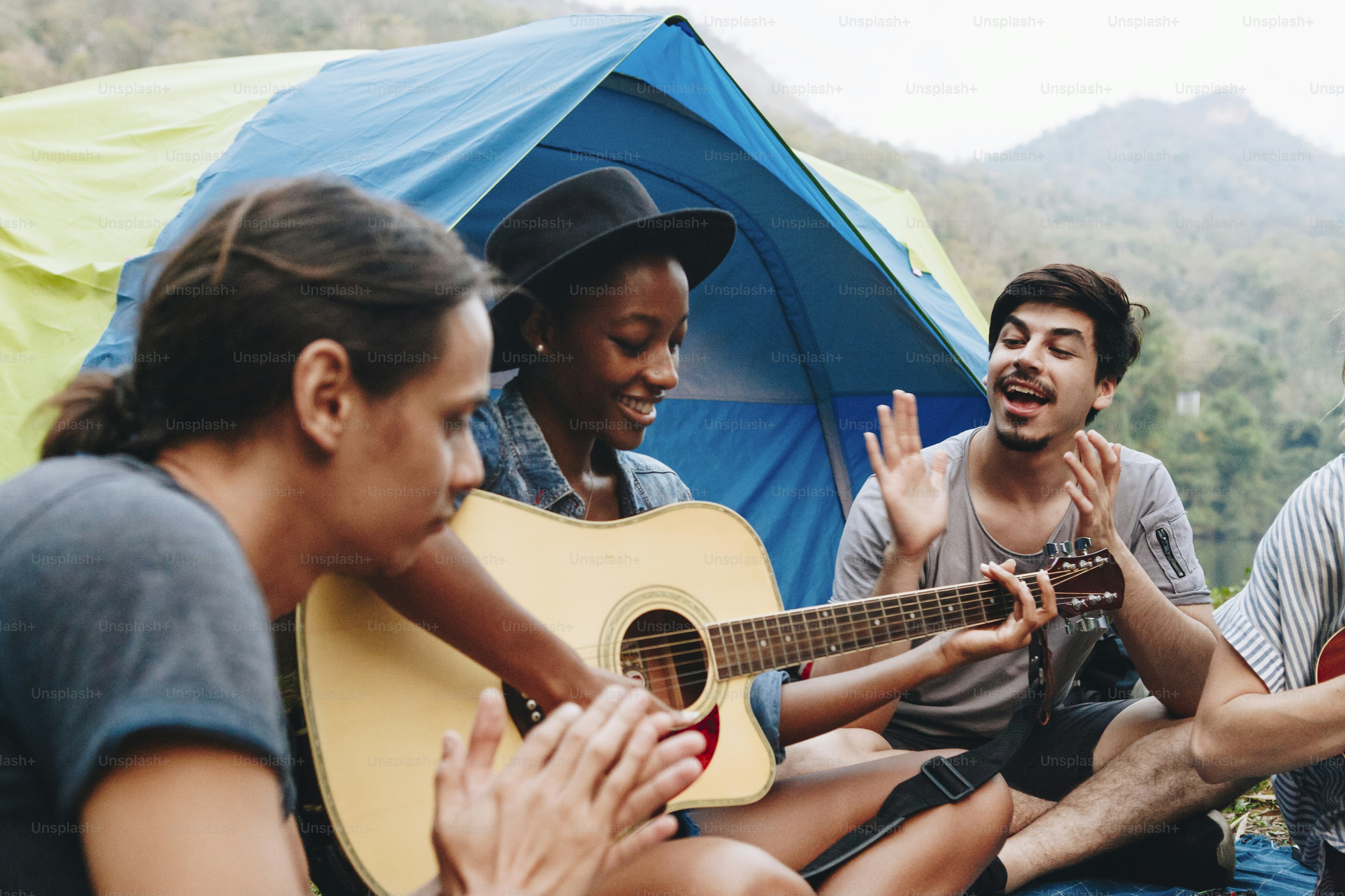 Group of young adult friends in camp site playing guitar