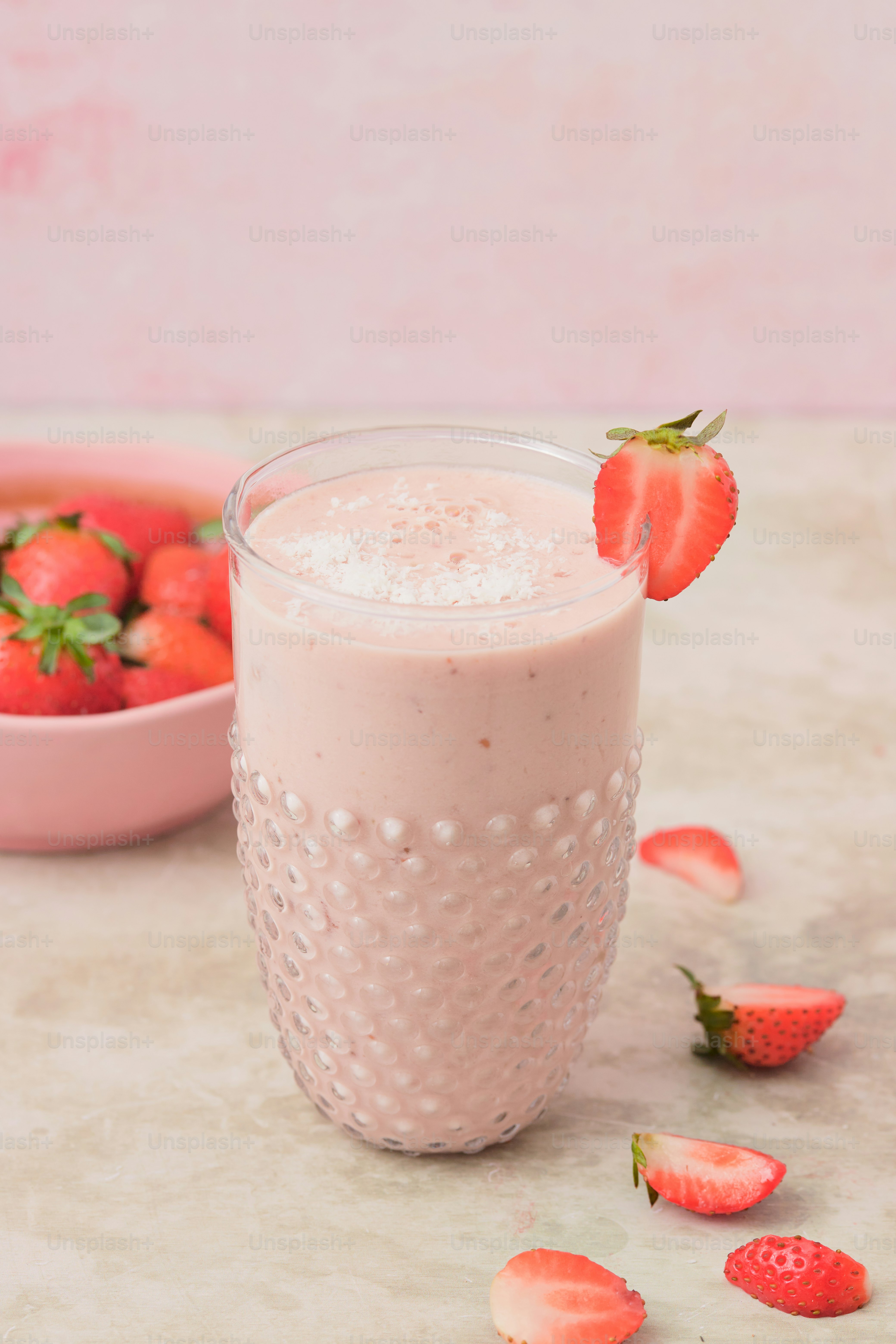 A glass of strawberry milk next to a bowl of strawberries