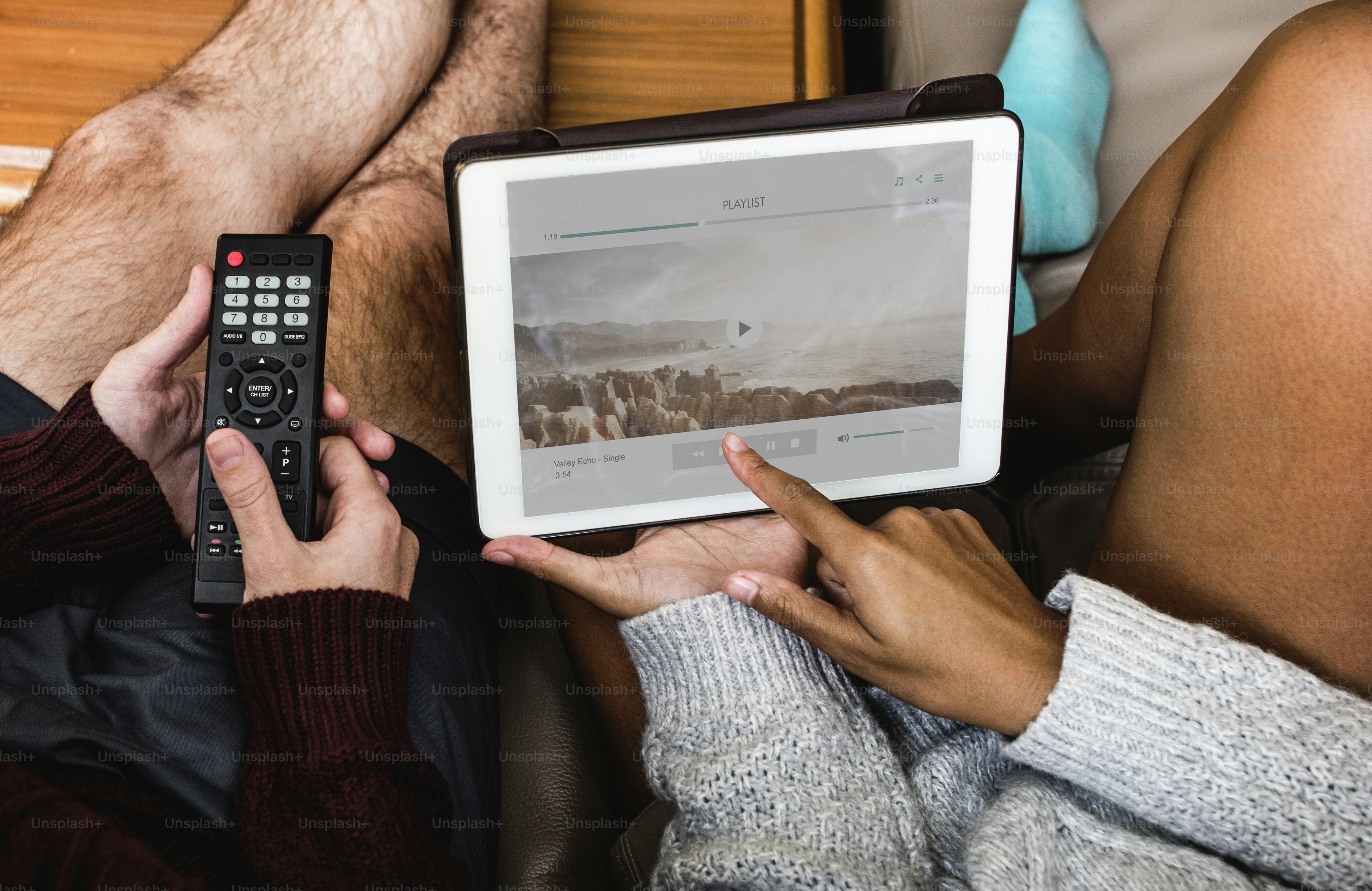 Dos personas en un sofá con un mando a distancia y una tablet poniendo música