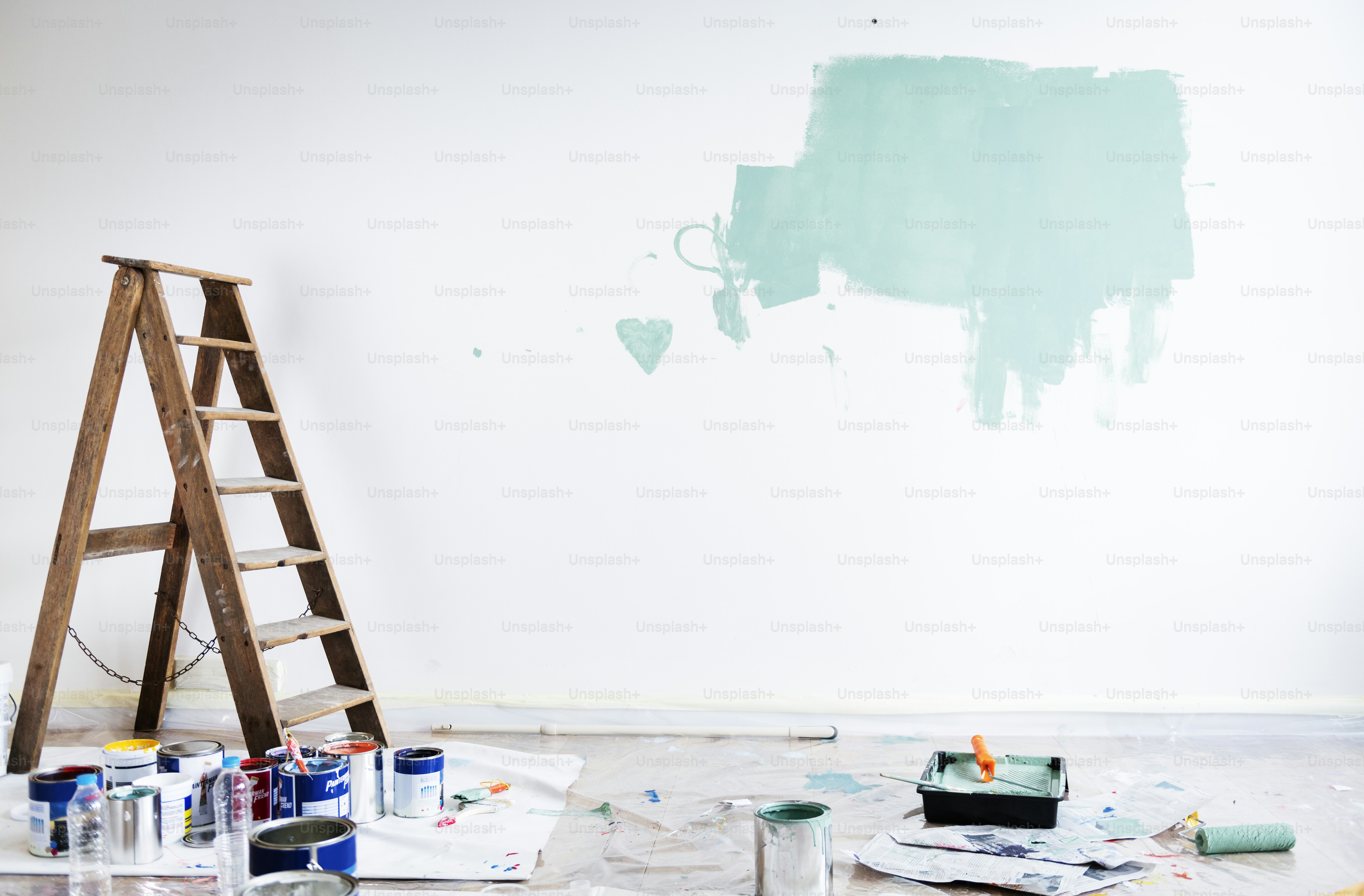 A wooden ladder beside a white wall with a patch of mint green paint