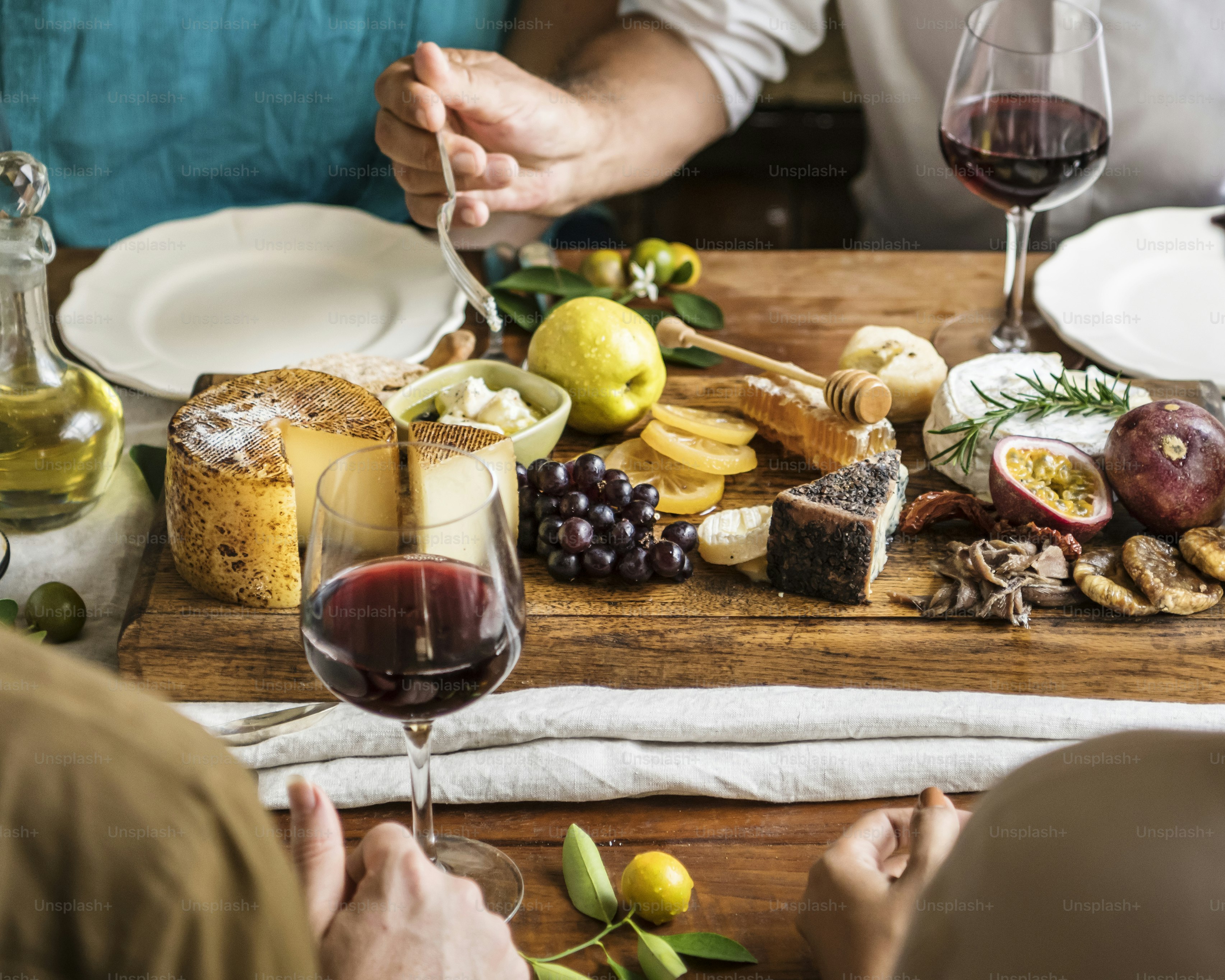 Des gens mangent un plateau de fromages avec des fruits de saison et du vin