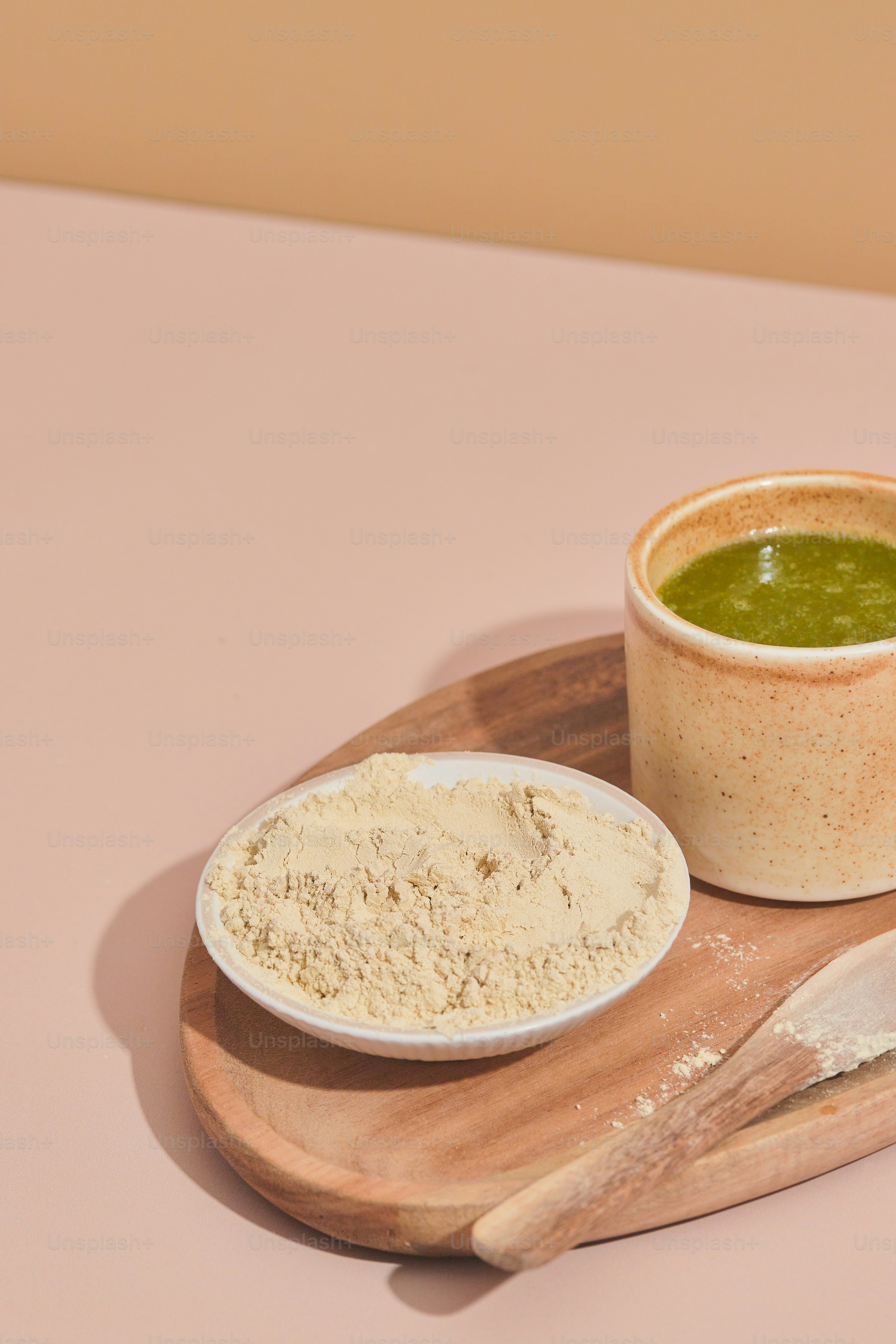 A bowl of green liquid next to a wooden spoon