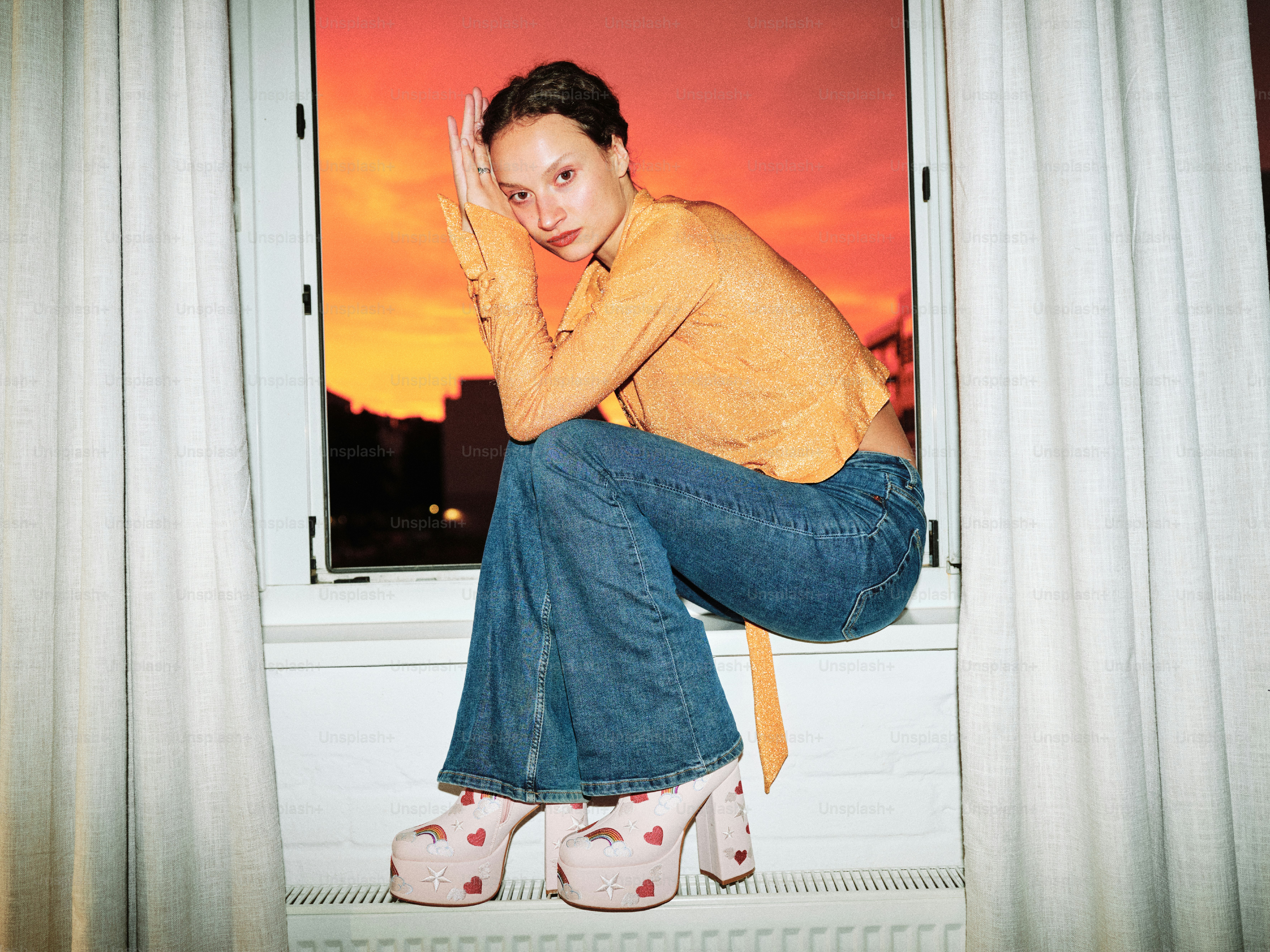 A woman sitting on a window sill in front of a sunset