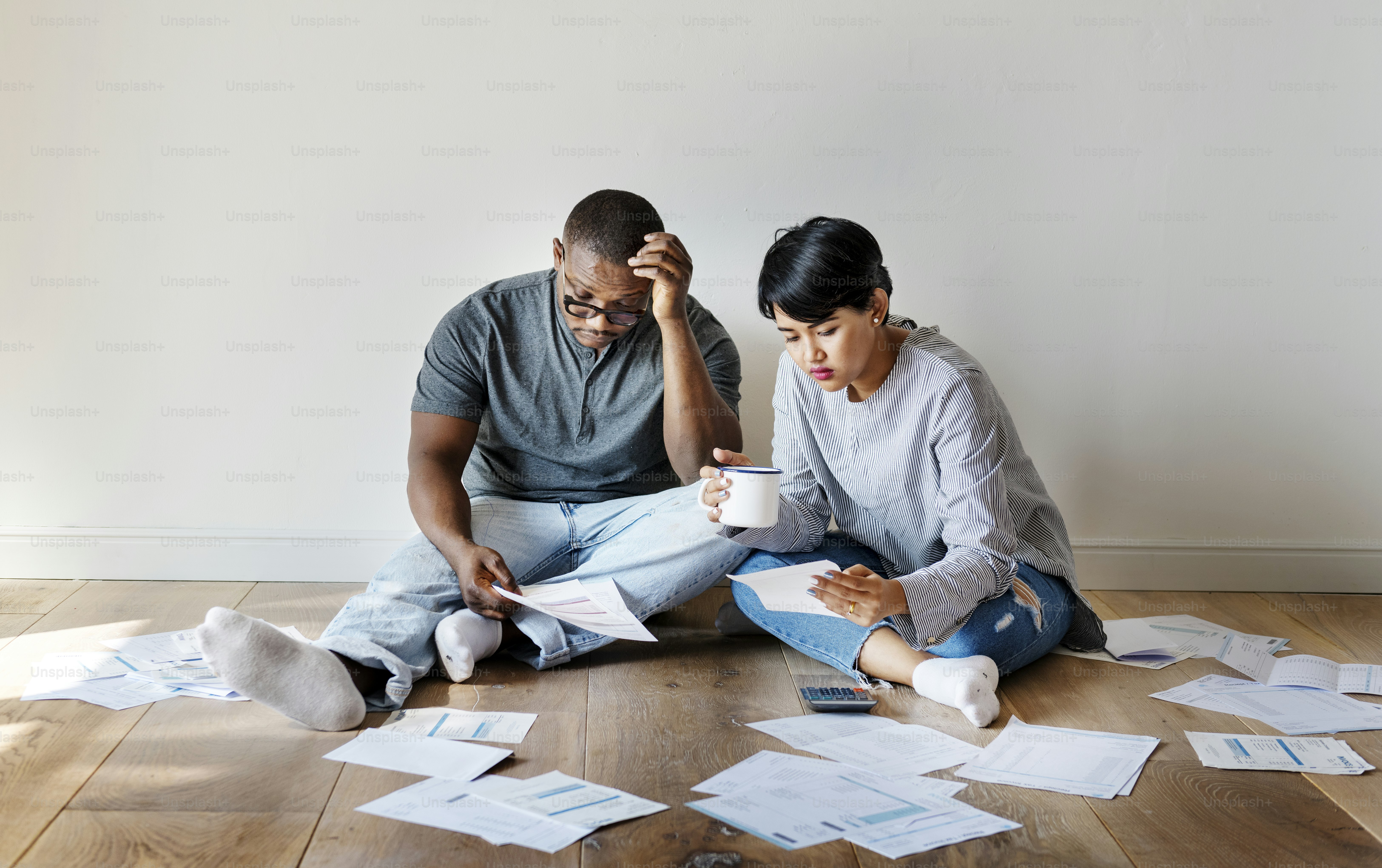 Two adults sitting on a wooden floor surrounded by scattered financial documents
