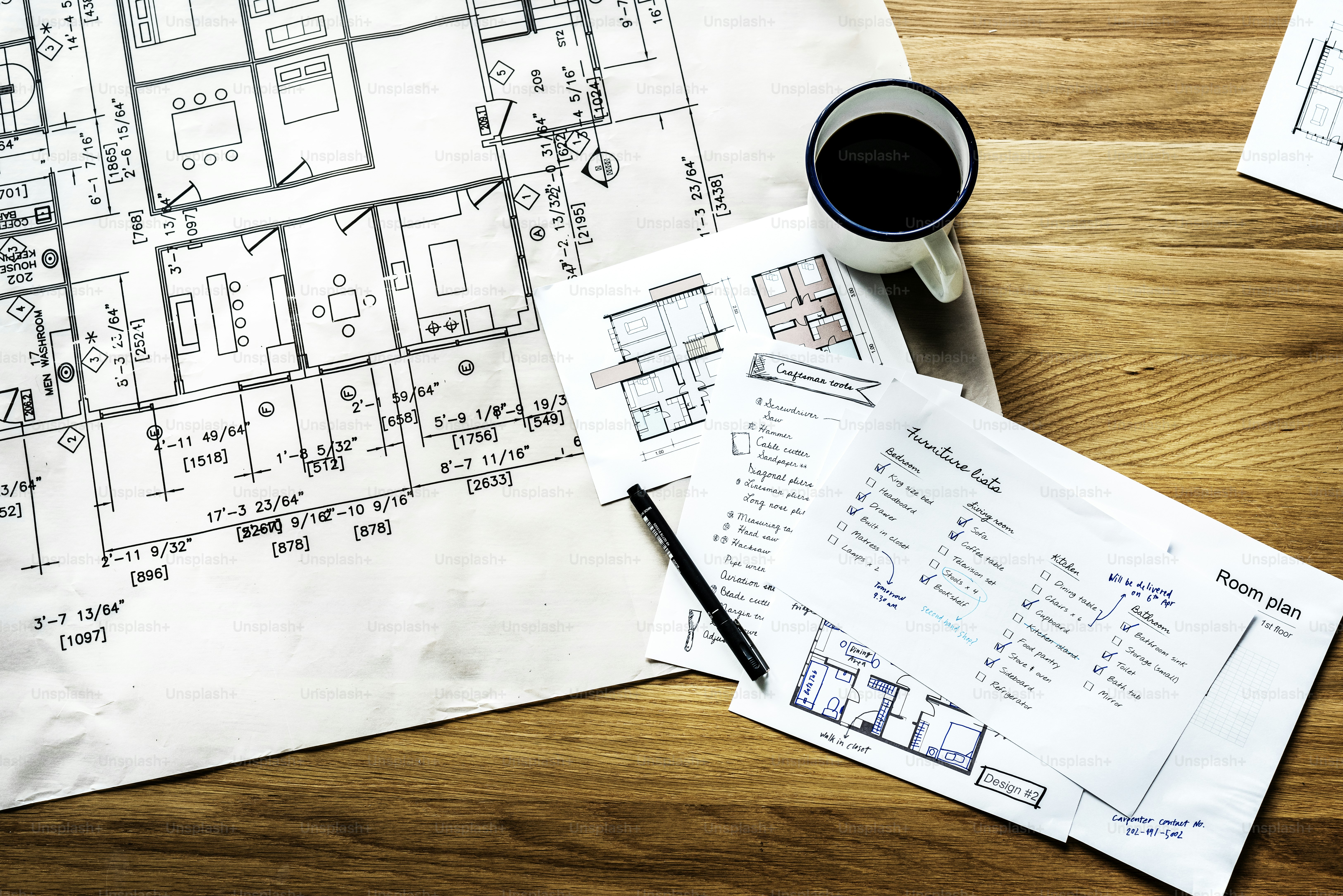 Architectural blueprints, a furniture checklist, a pen, and a coffee mug on wood