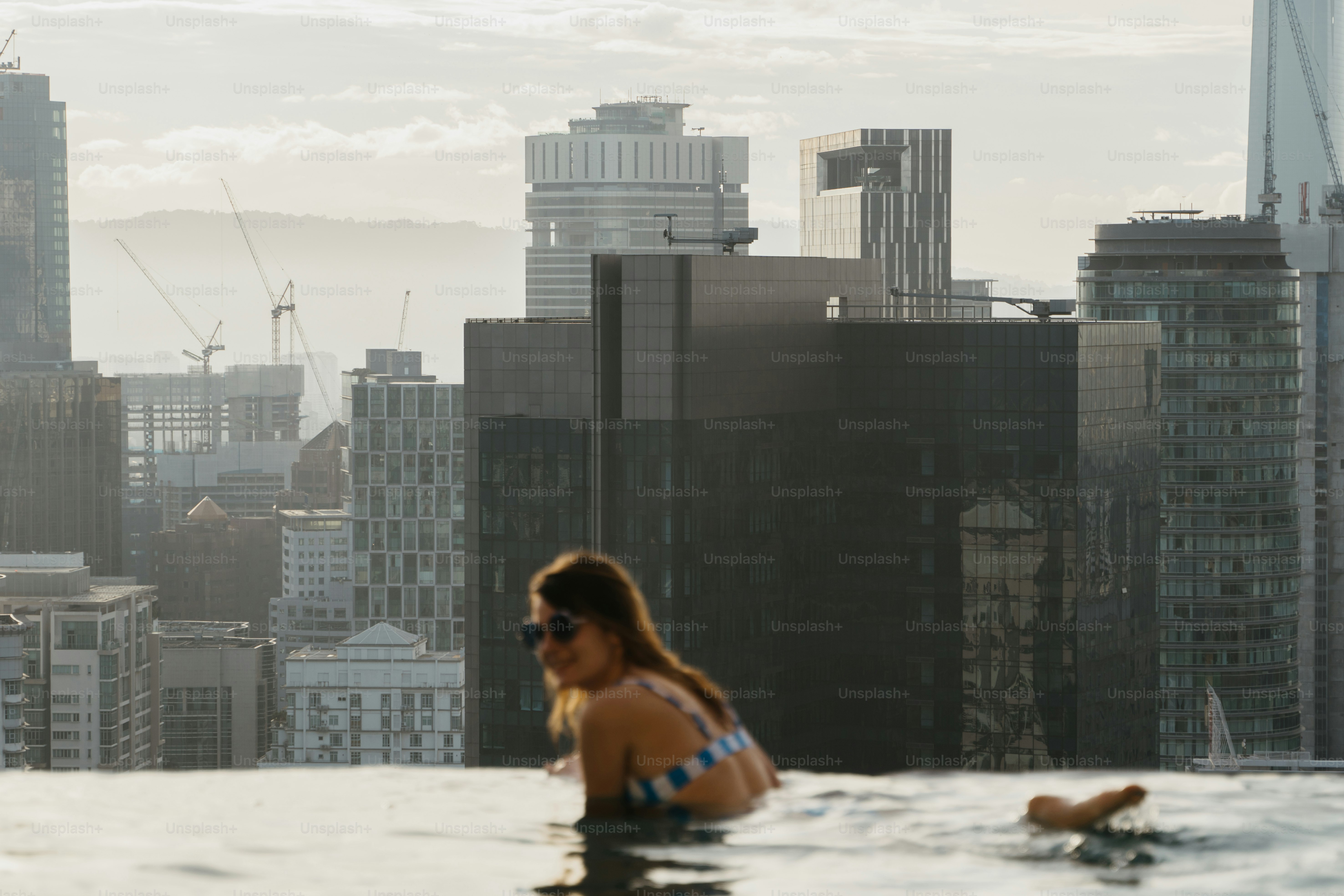 A woman in a bikini sitting in a pool in front of a cityscape