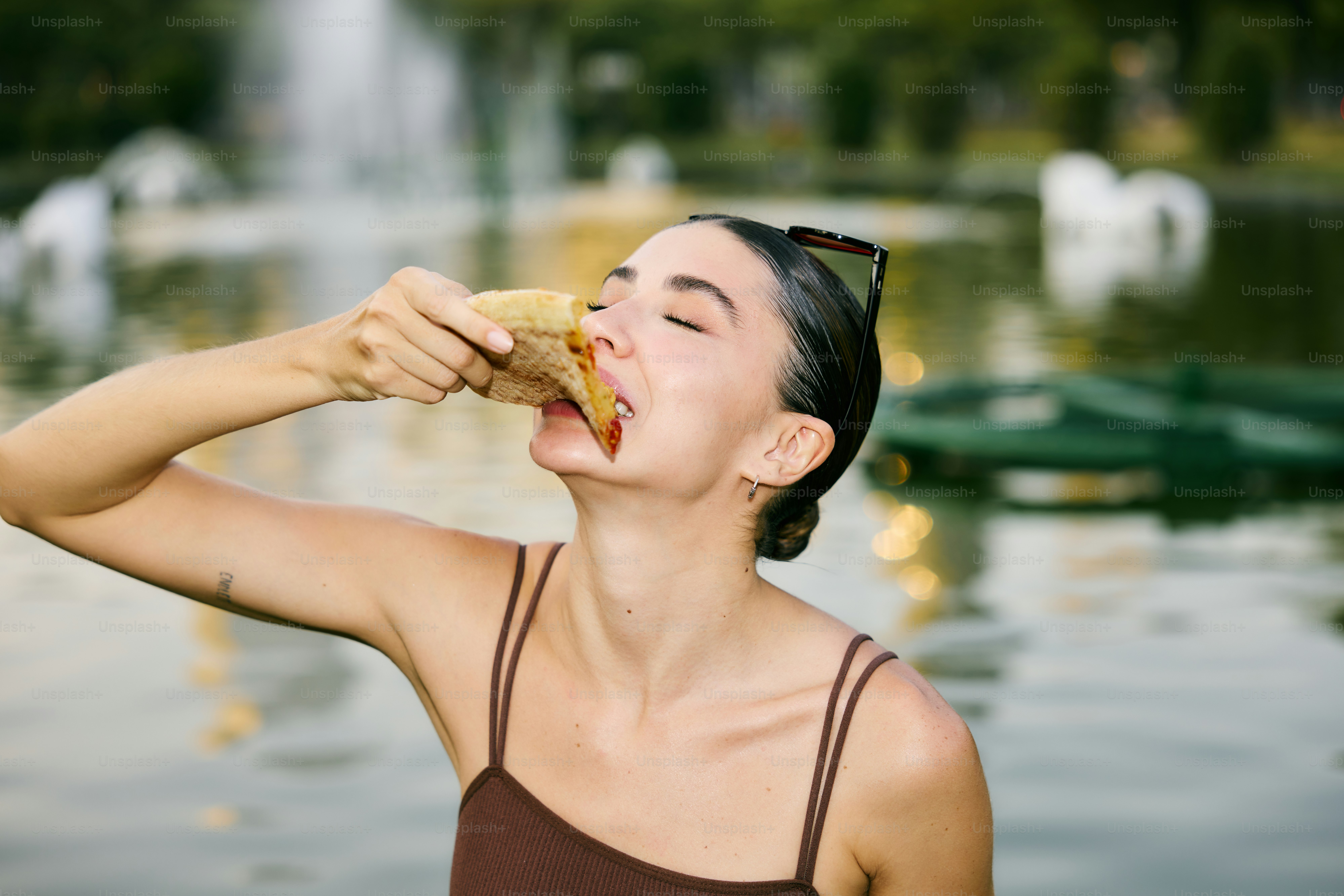 A woman eating a sandwich in front of a fountain