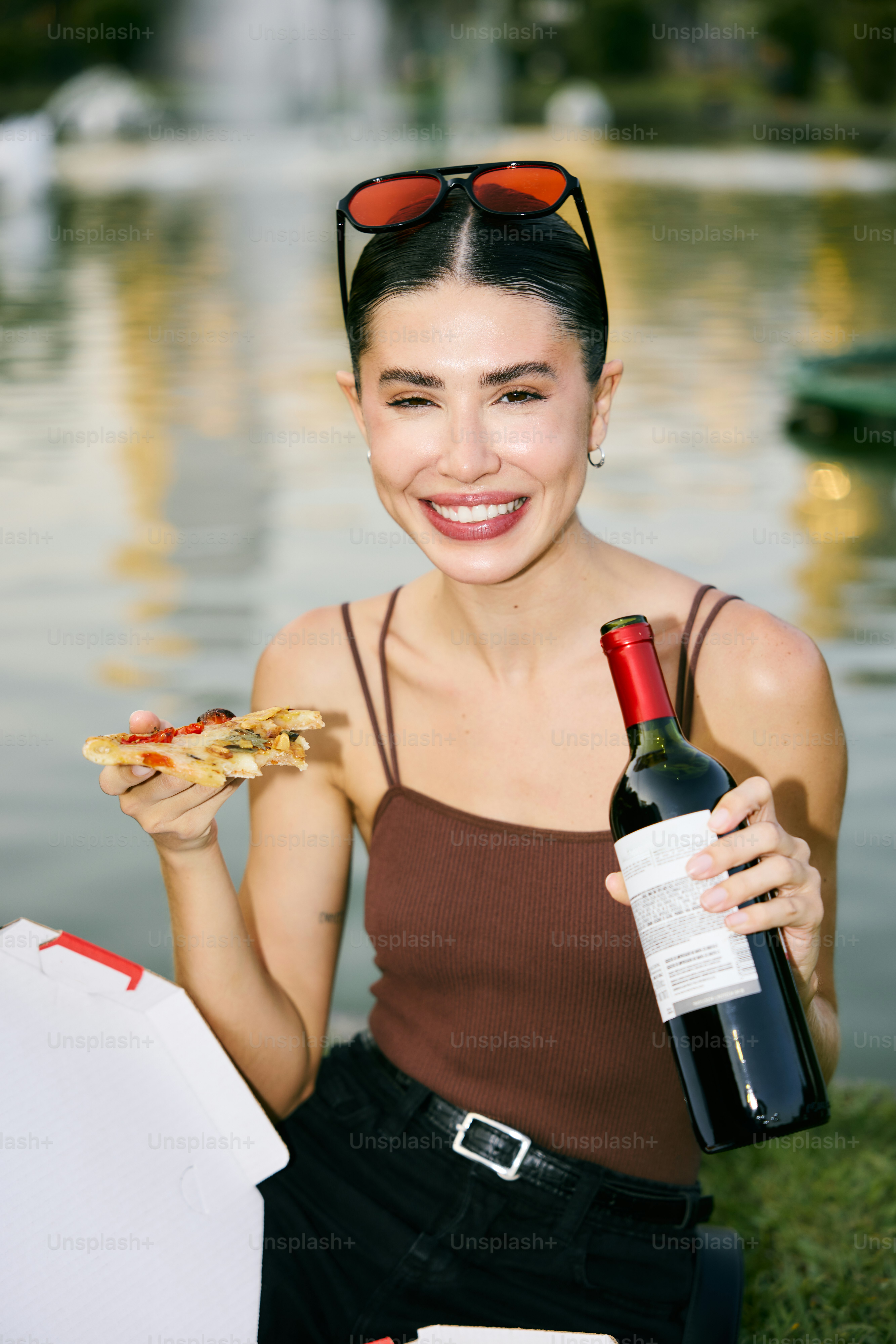 A woman holding a bottle of wine and a slice of pizza