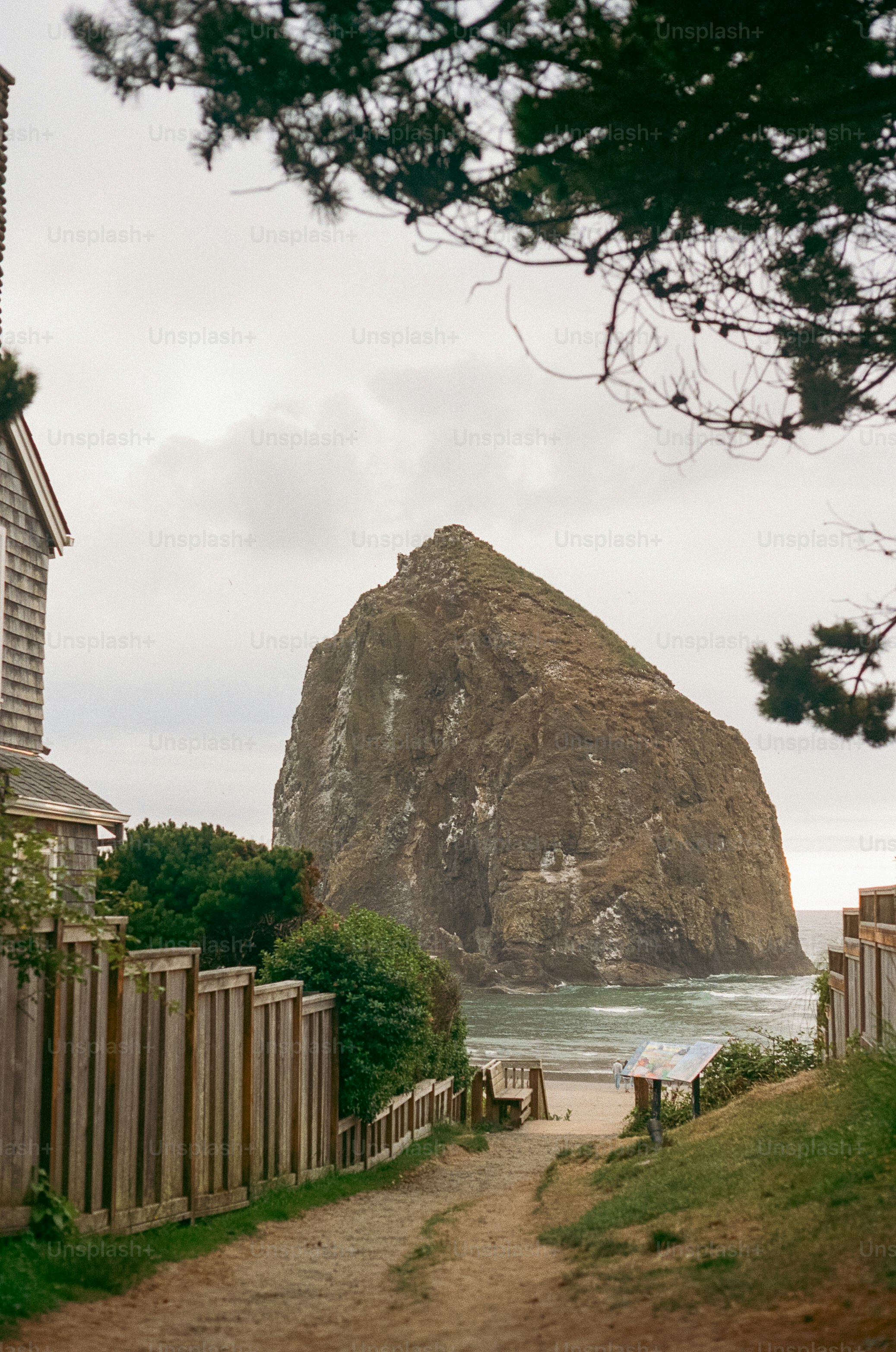 A path leading to a beach with a large rock in the background