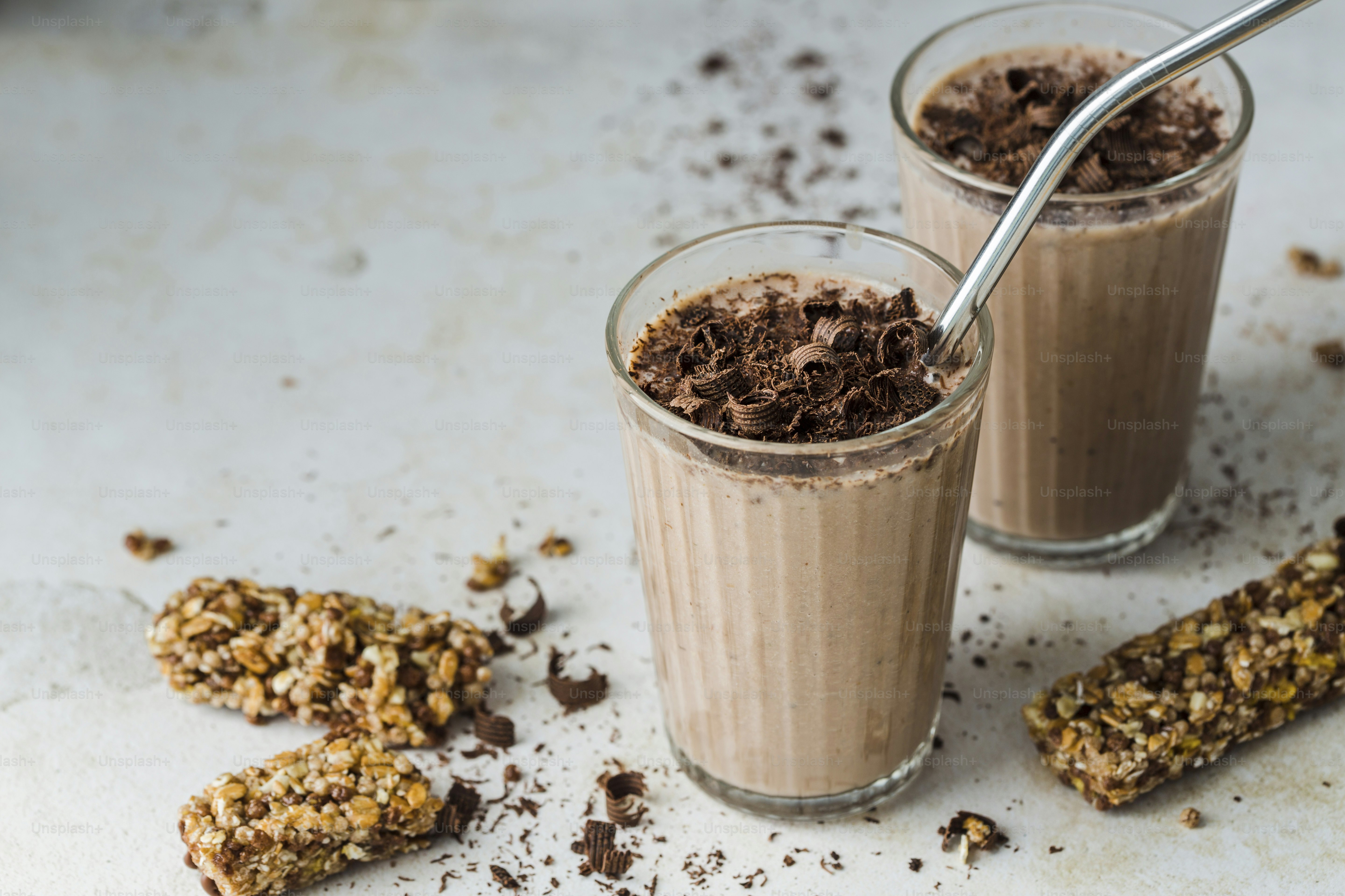 Two glasses of chocolate milkshake with granola on the side