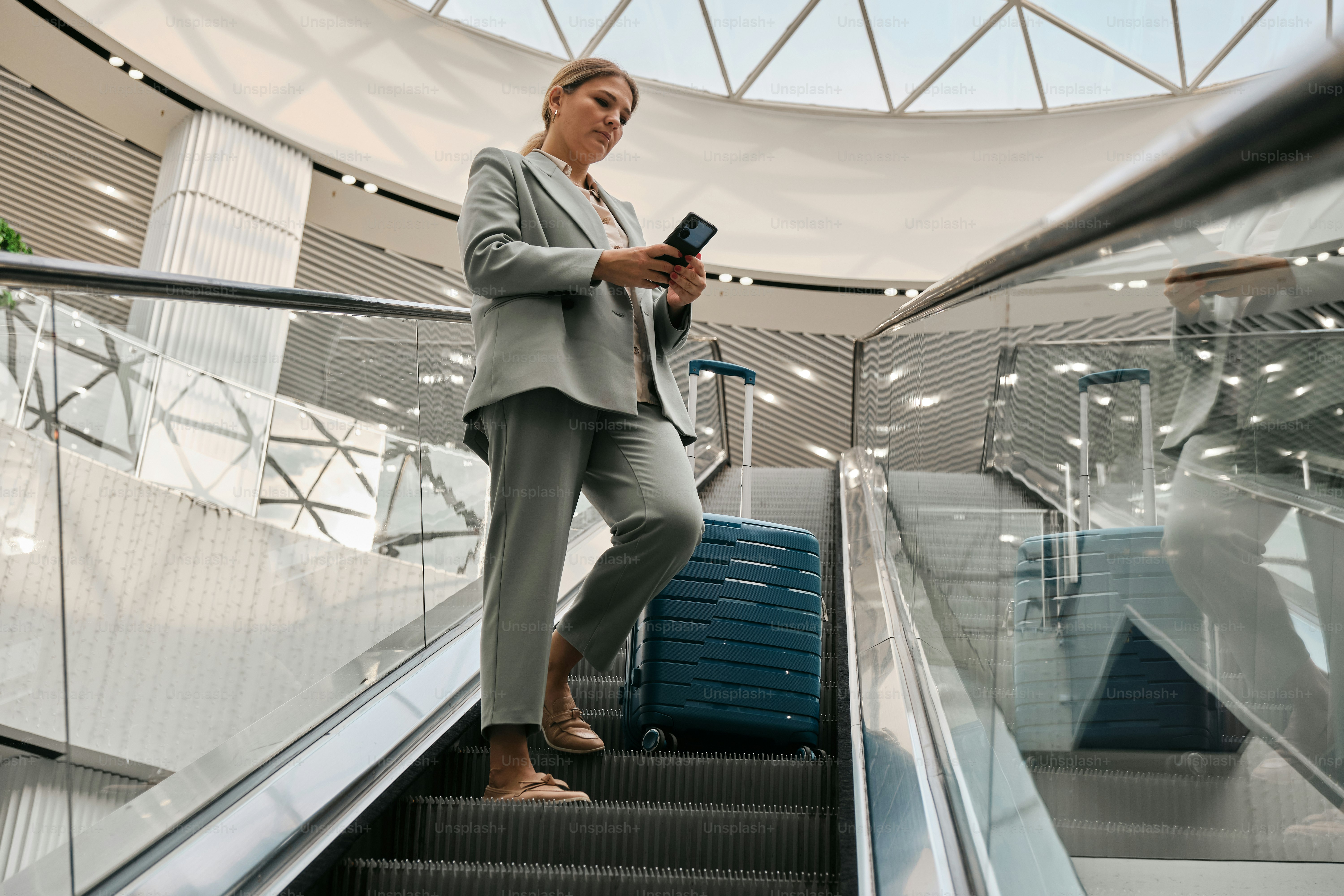 A woman is standing on an escalator with her luggage