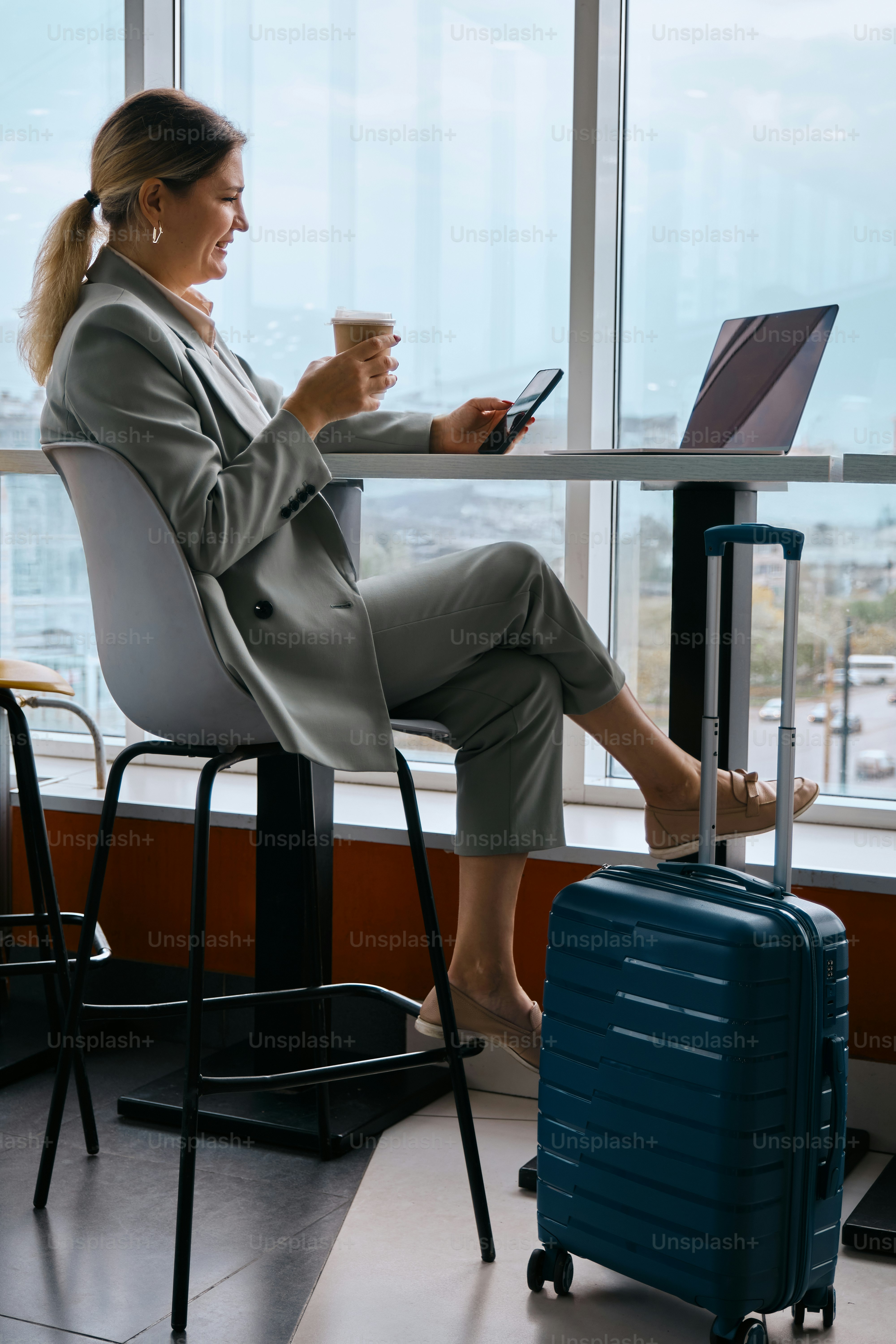 A woman sitting at a table with a laptop and a suitcase