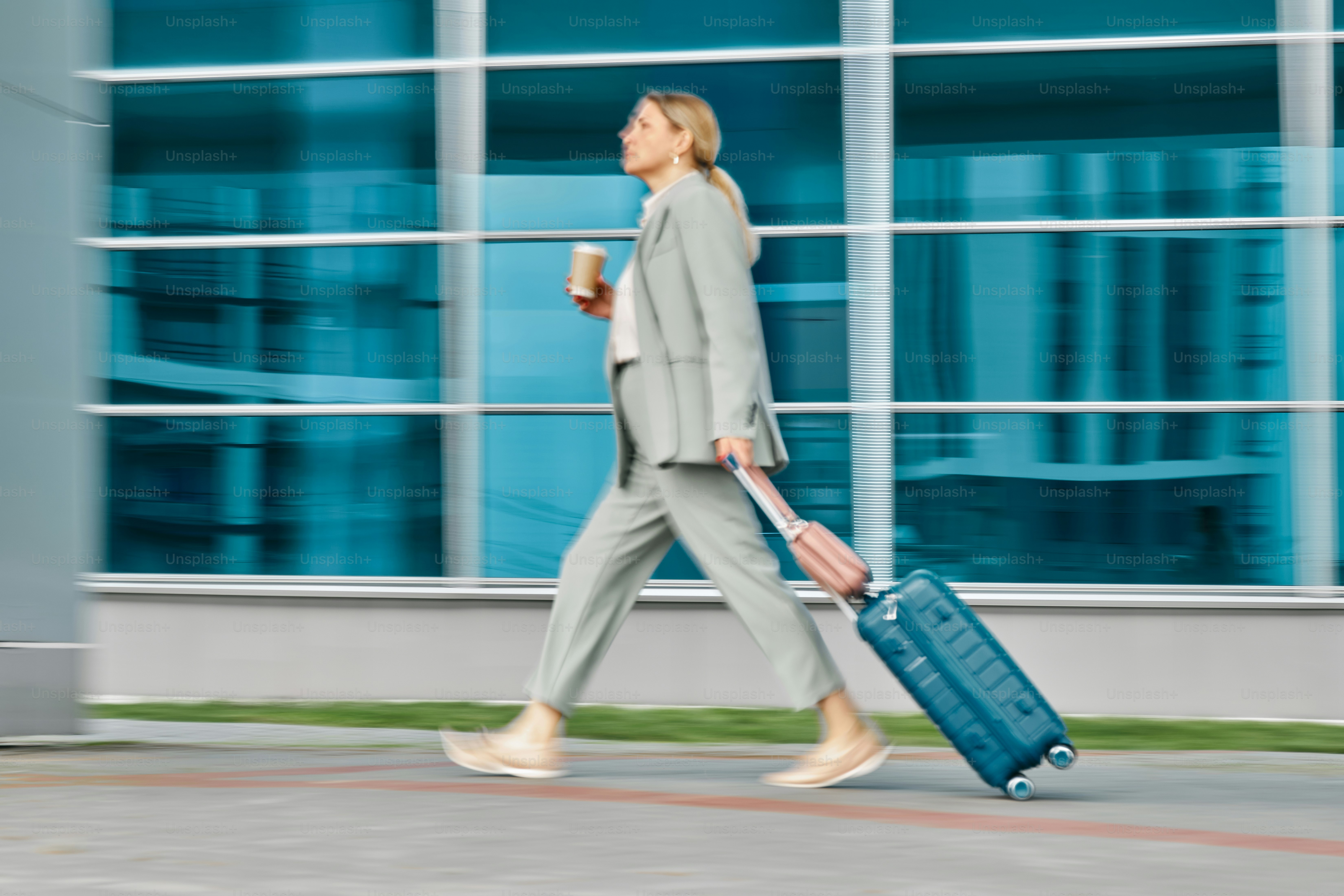 A woman walking down a street with a suitcase and a cup of coffee