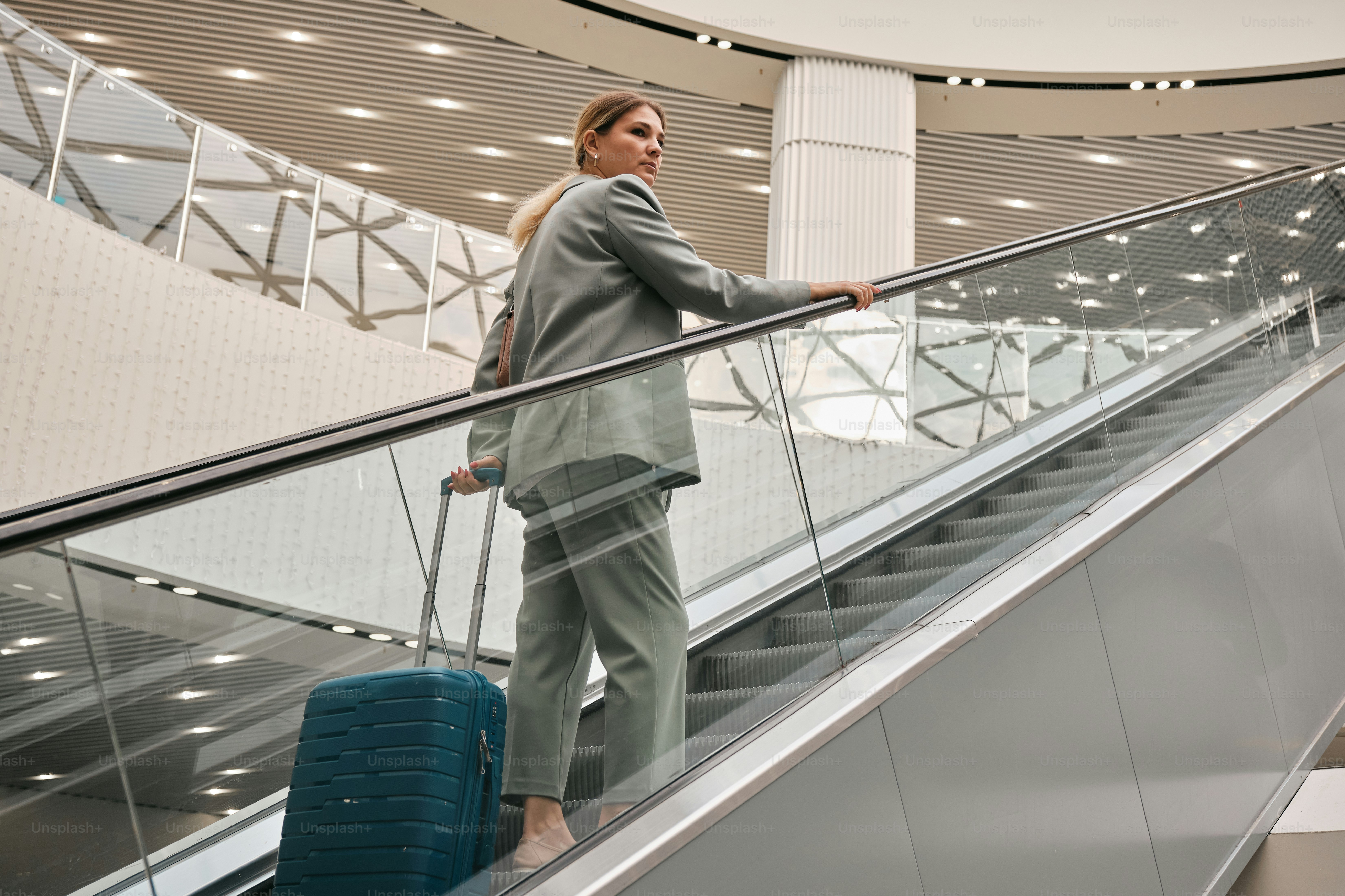 A woman is standing on an escalator with her luggage