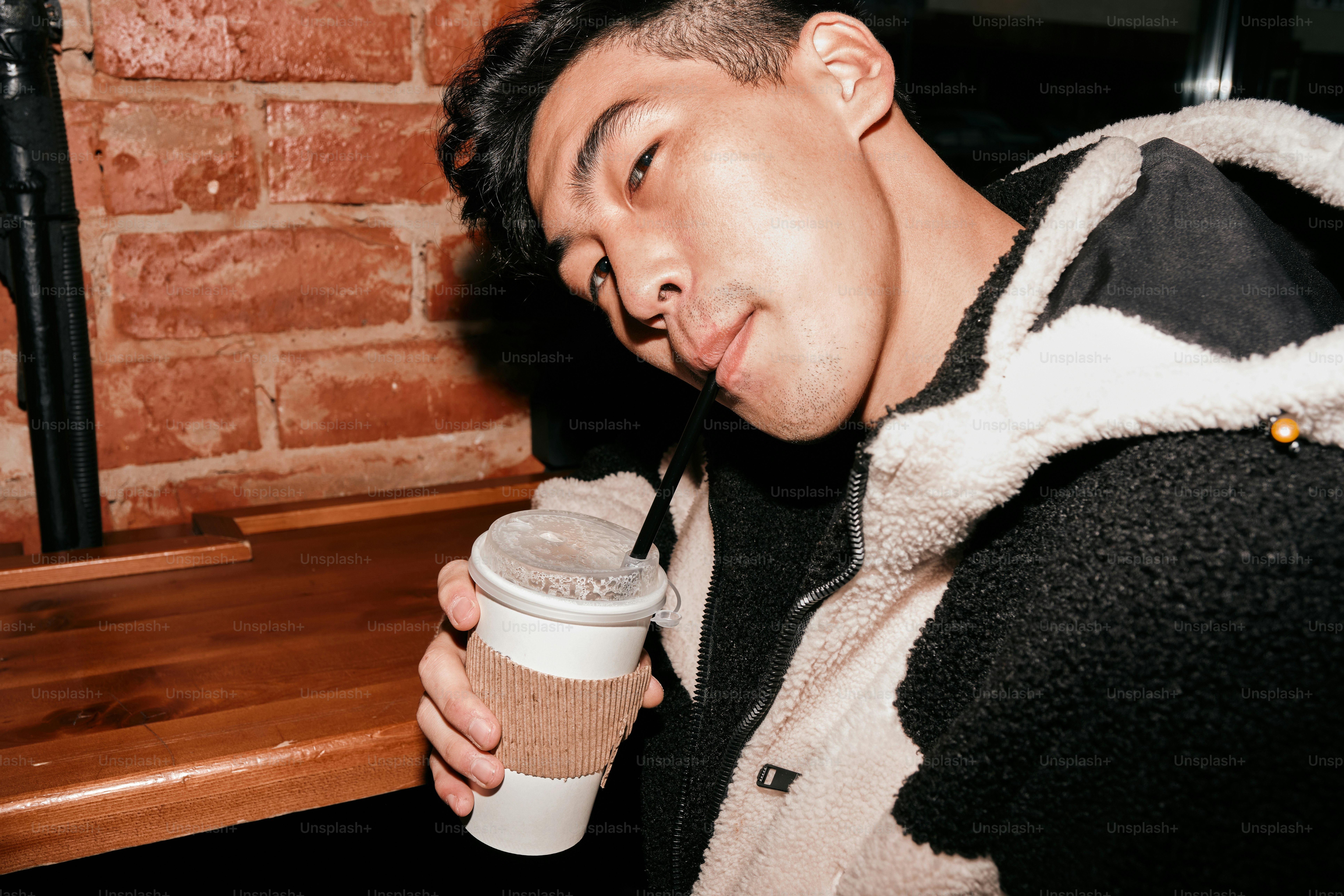 A man holding a cup of coffee in front of a brick wall