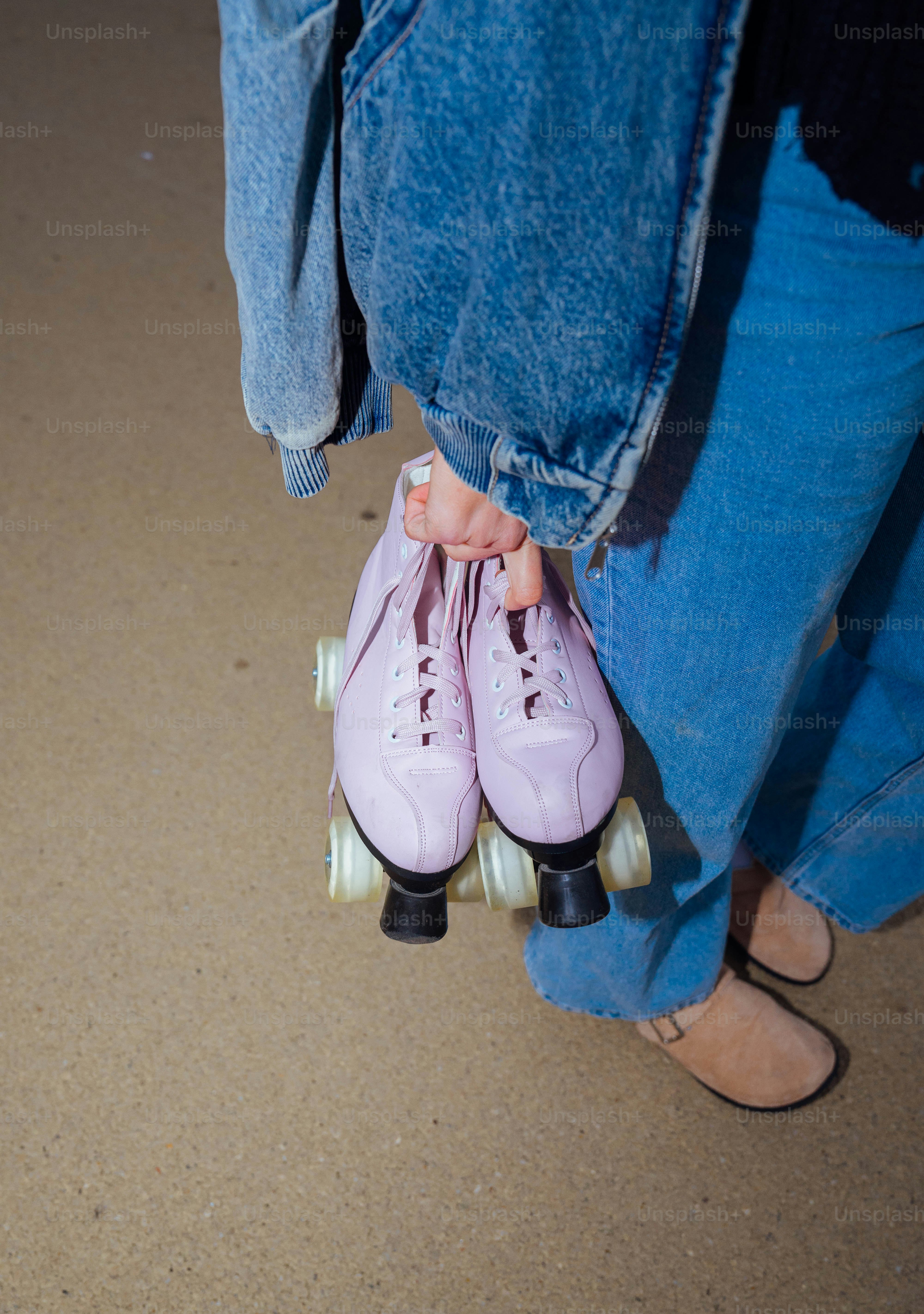 A pair of pink roller skates being held by a person