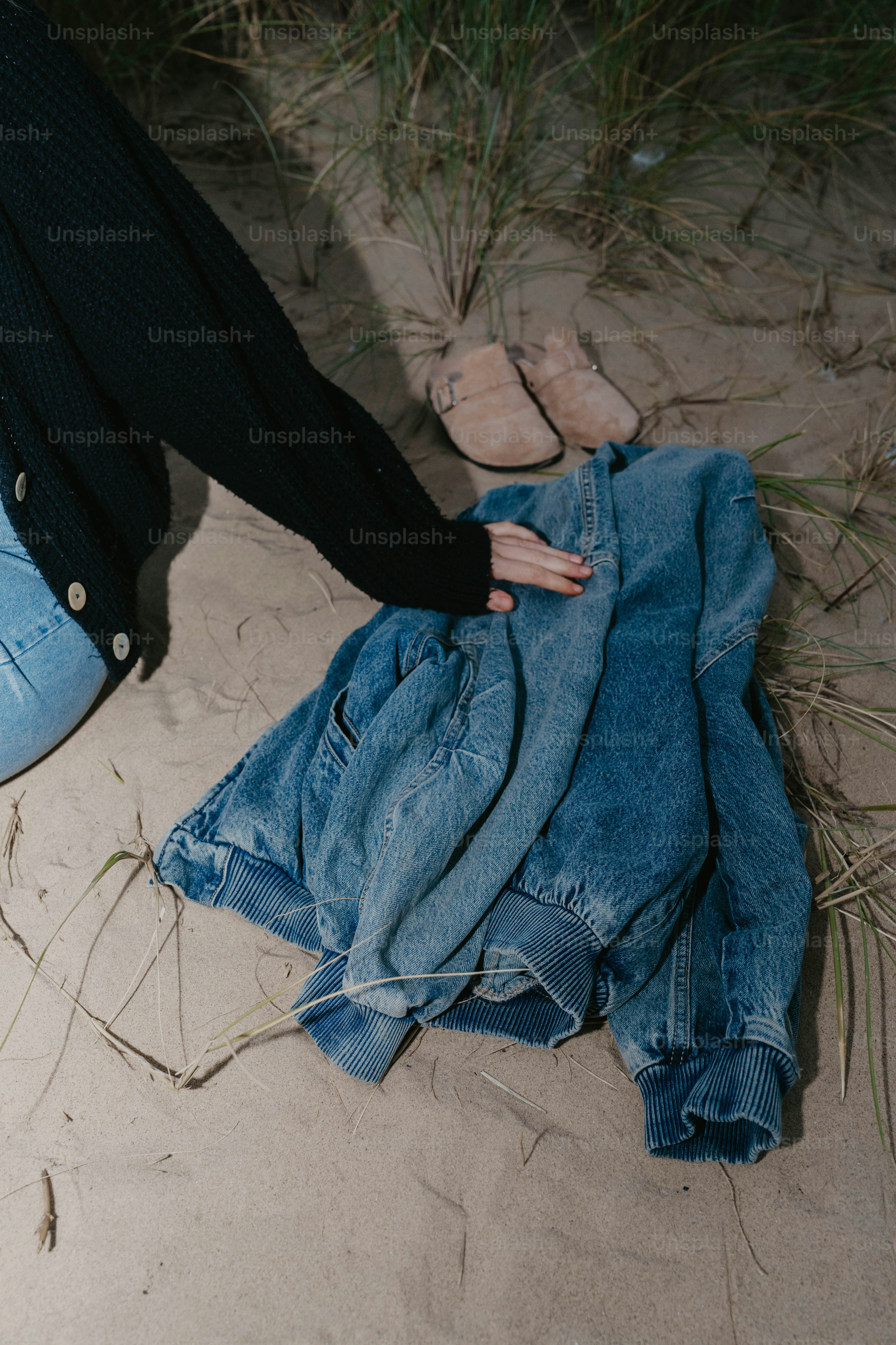 A pair of jeans and a jacket laying on the sand