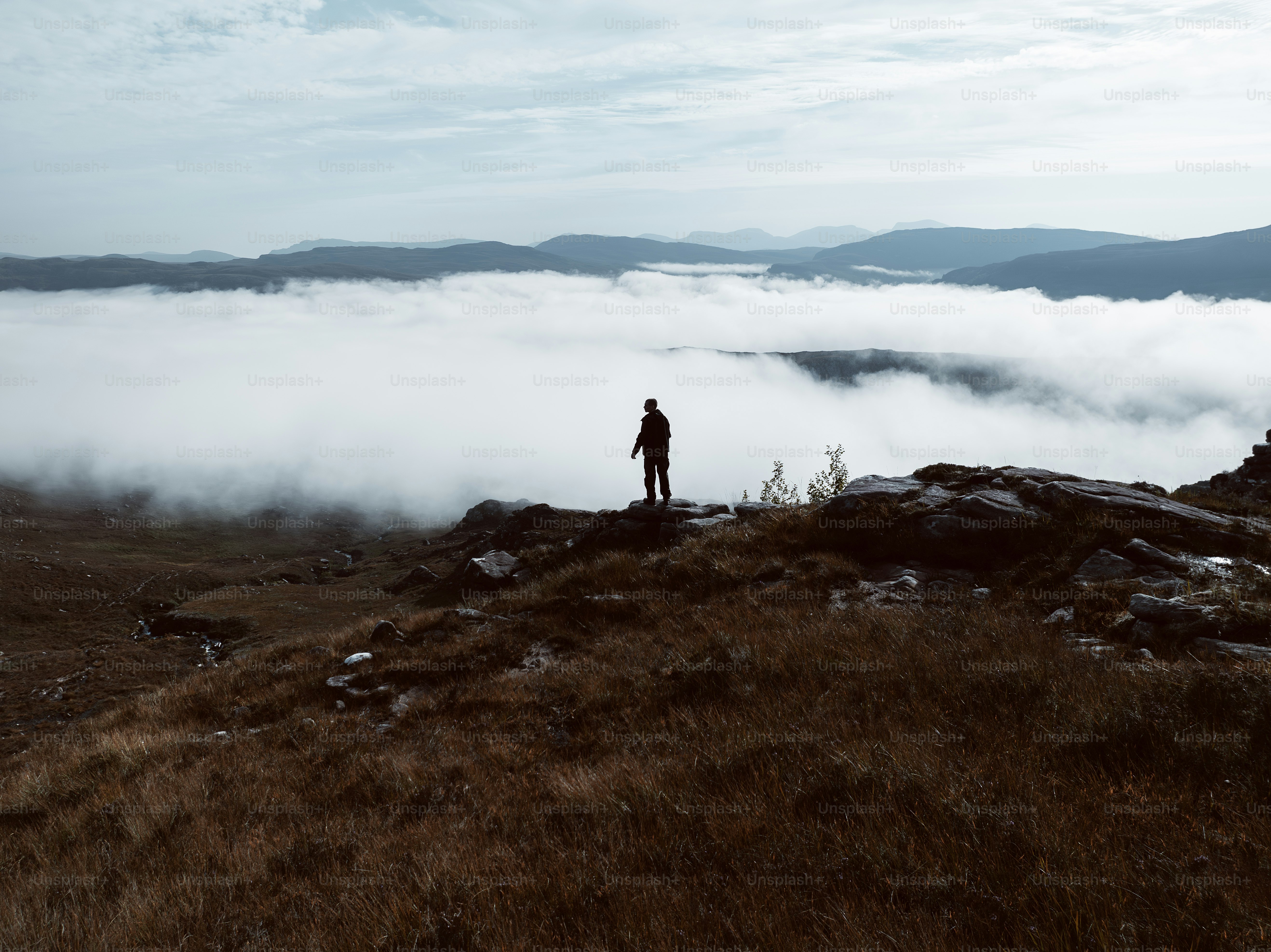 A person standing on top of a hill surrounded by clouds