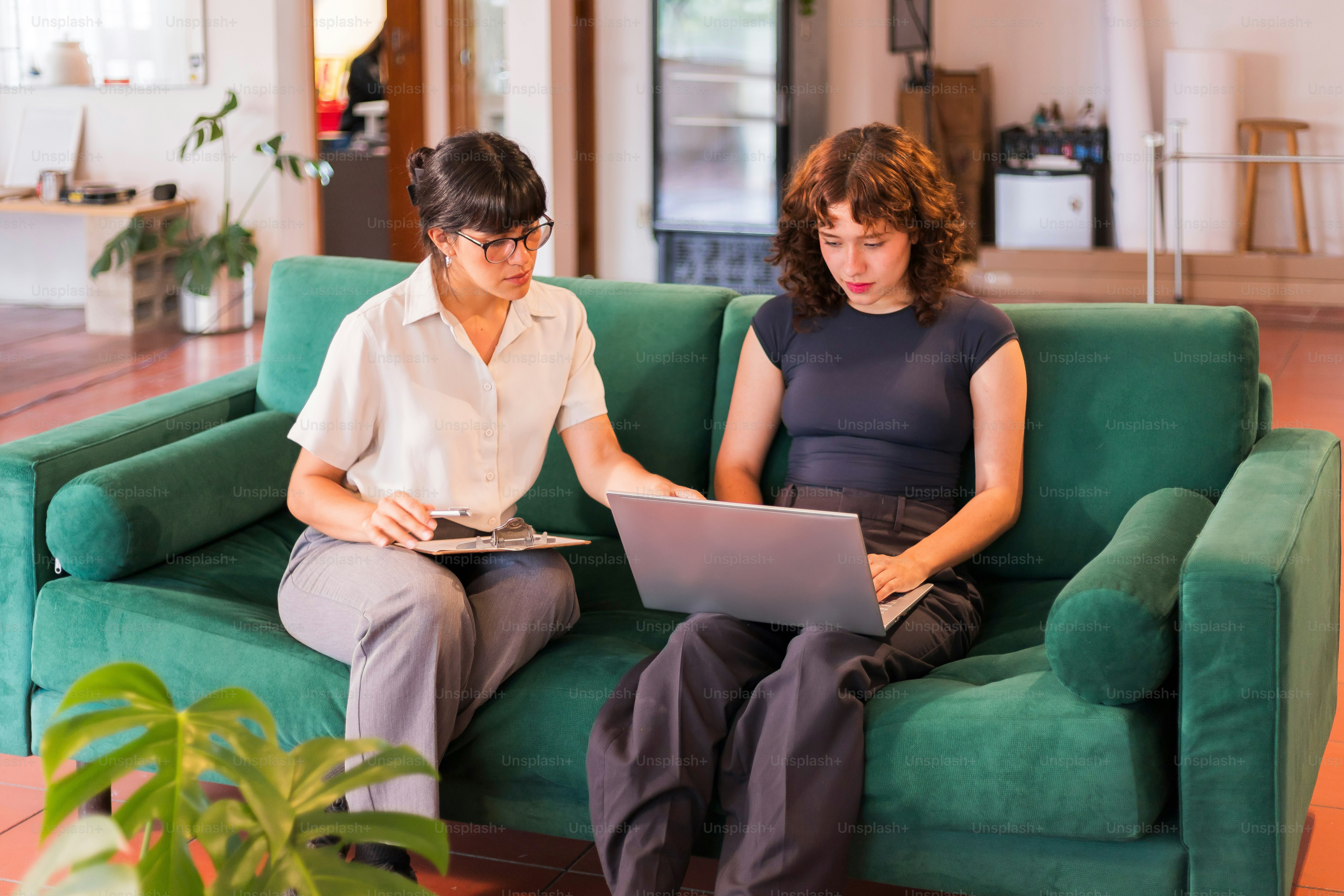 Deux femmes assises sur un canapé vert à l’aide d’ordinateurs portables