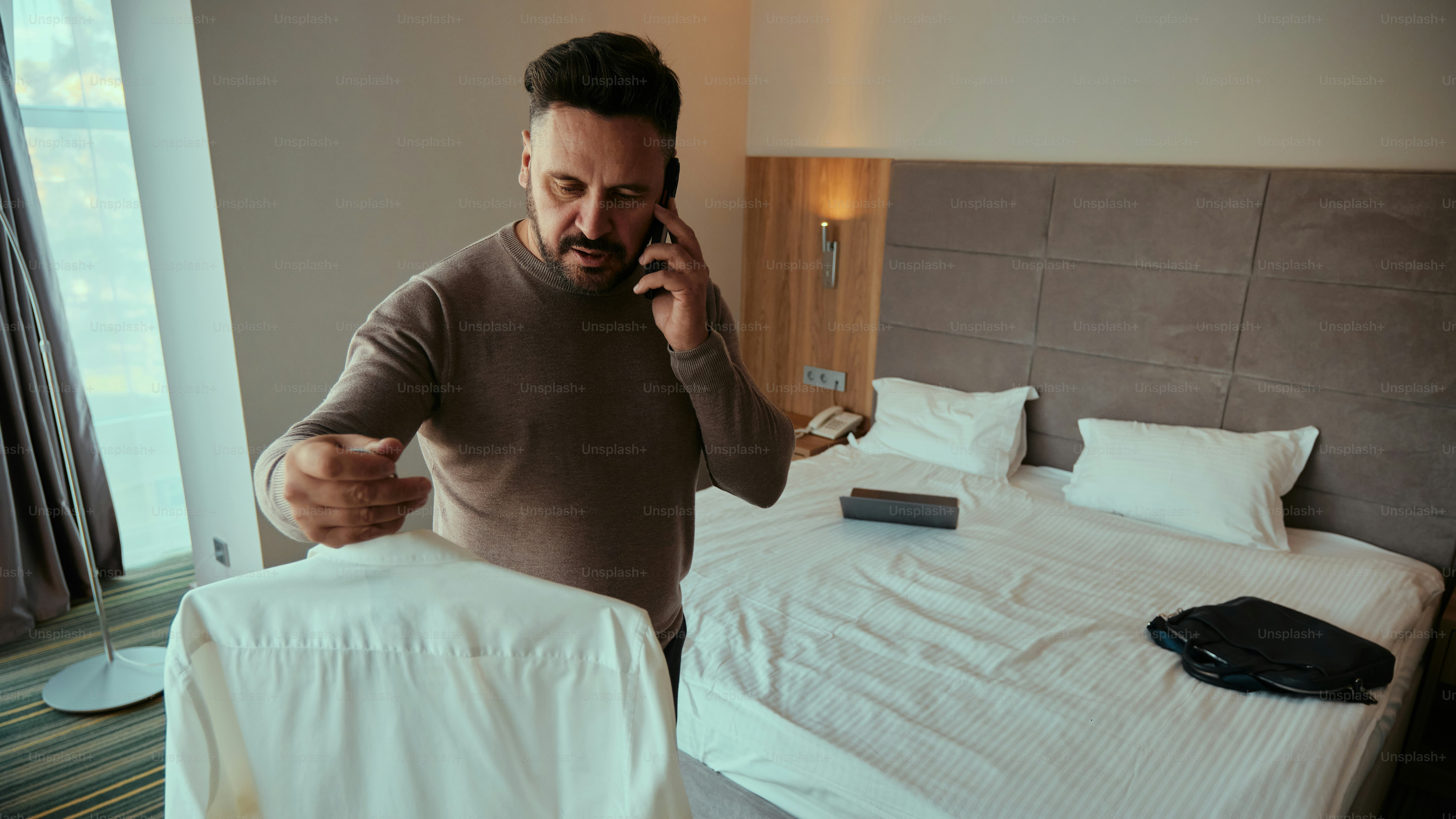 Ein Mann, der in einem Hotelzimmer steht und mit einem Handy telefoniert