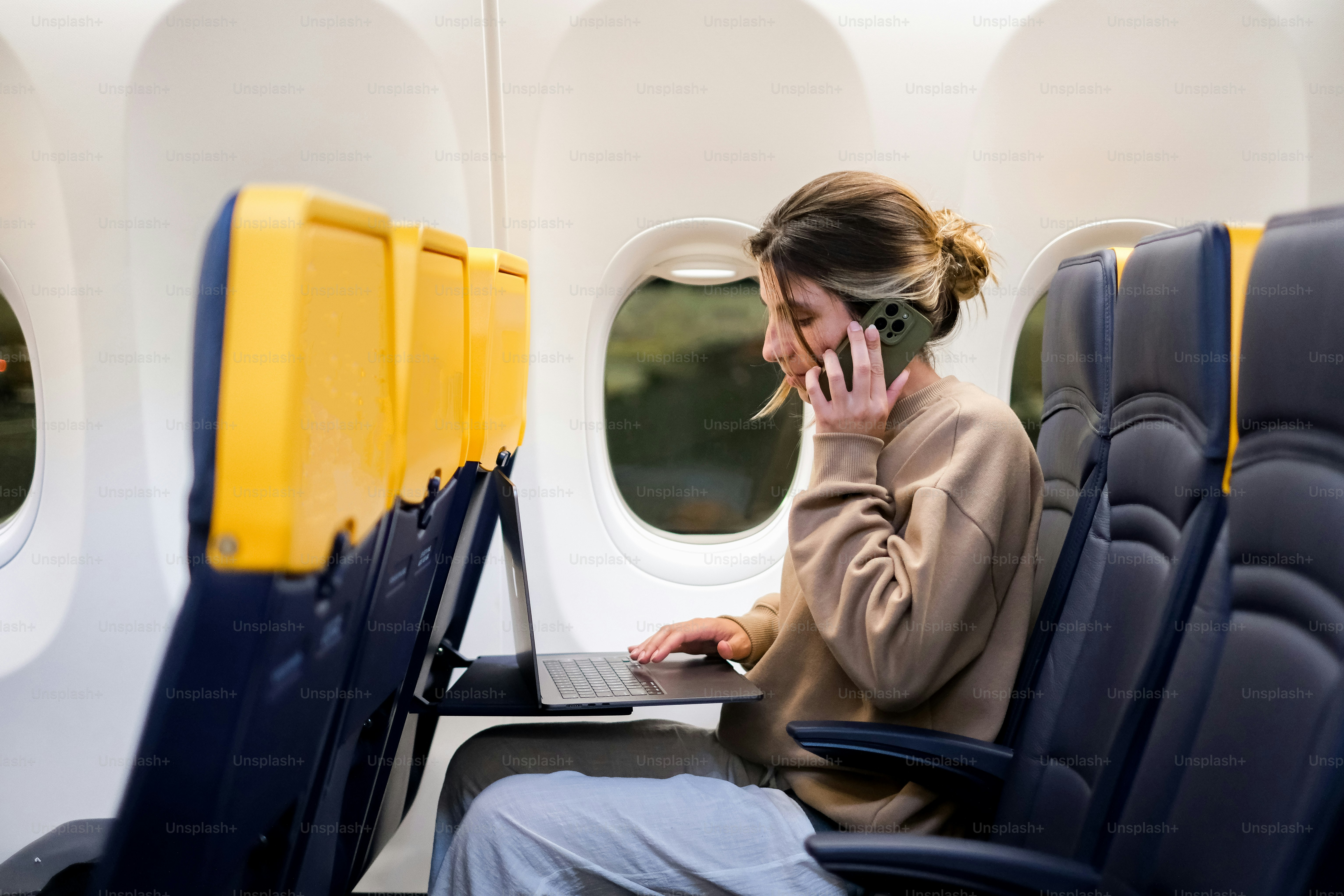 A woman sitting on an airplane talking on a cell phone