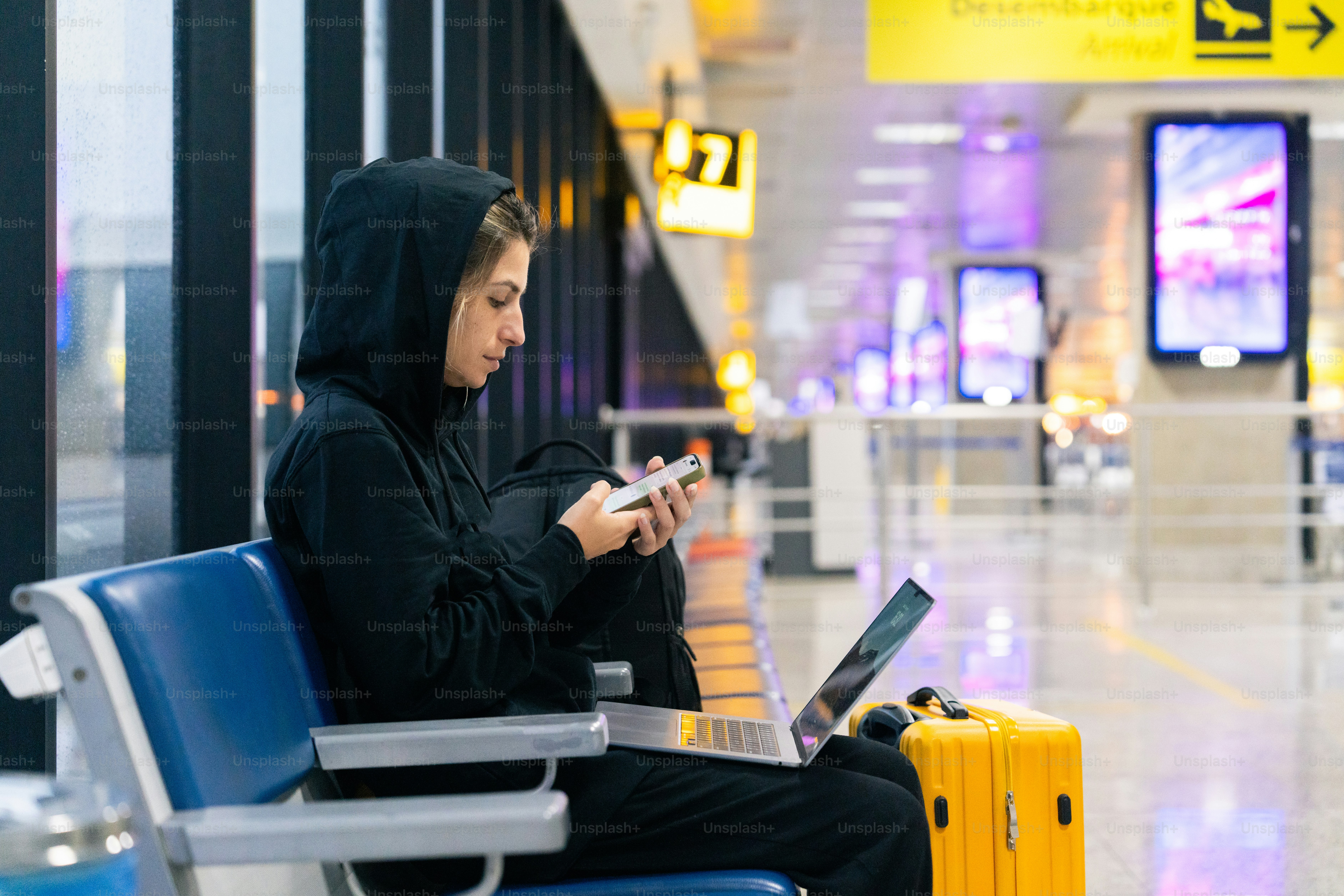 A woman sitting on a bench in an airport looking at her cell phone