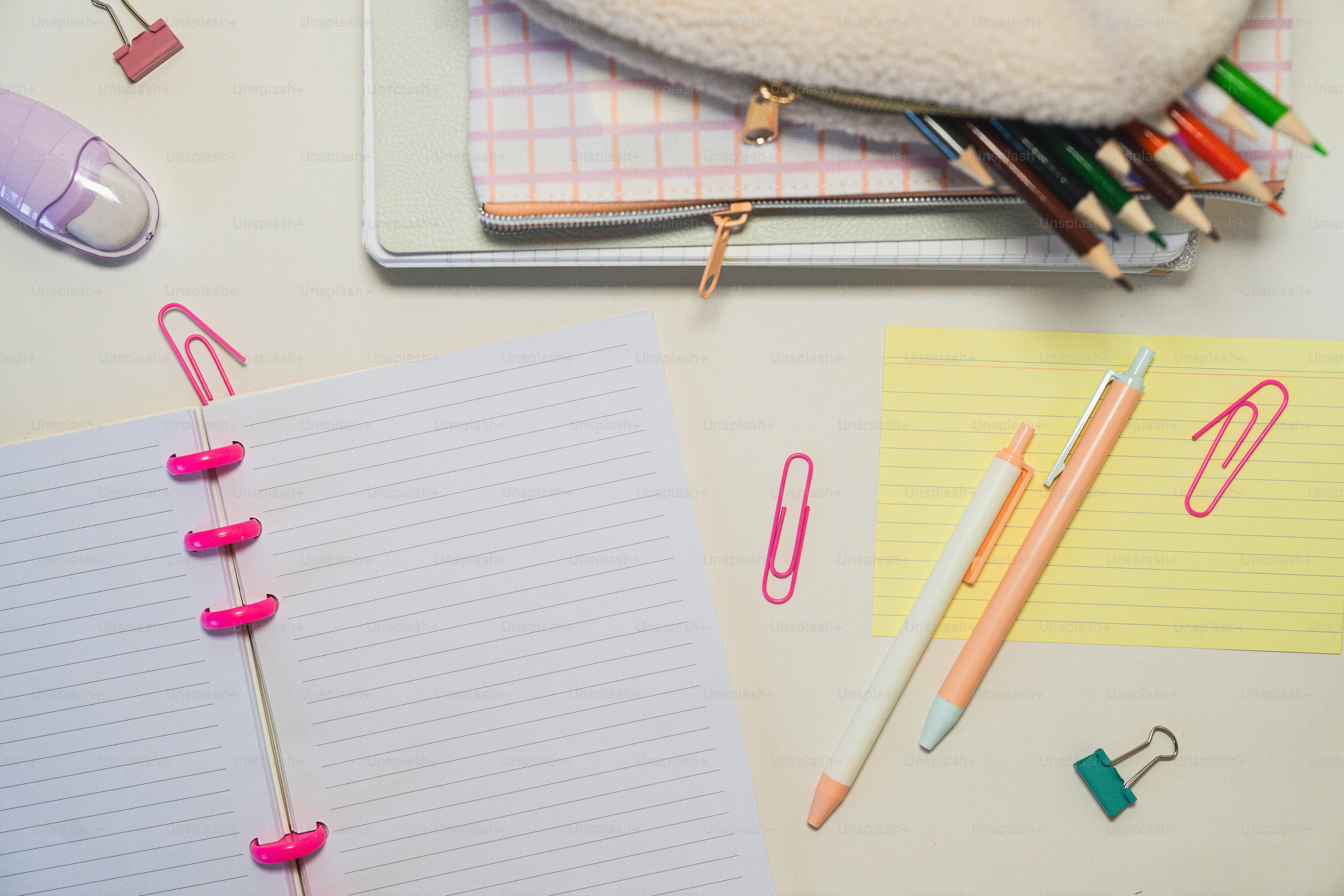 A table topped with notebooks, pens, and paper clips
