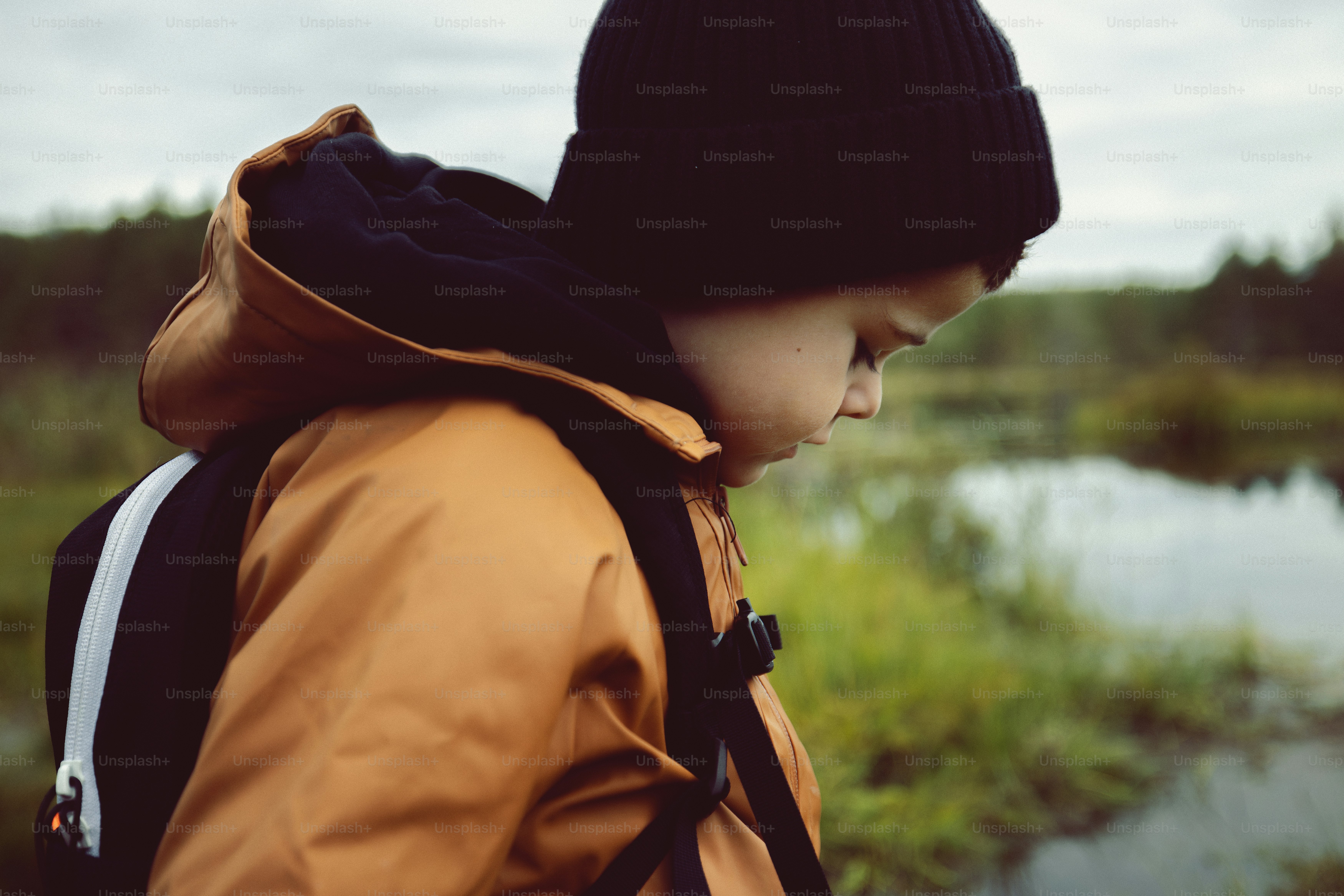 A young boy with a backpack looking at a pond