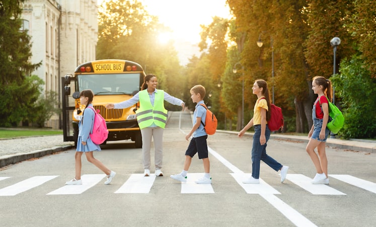 Children crossing a crosswalk on their way to school with a crossing guard holding traffic