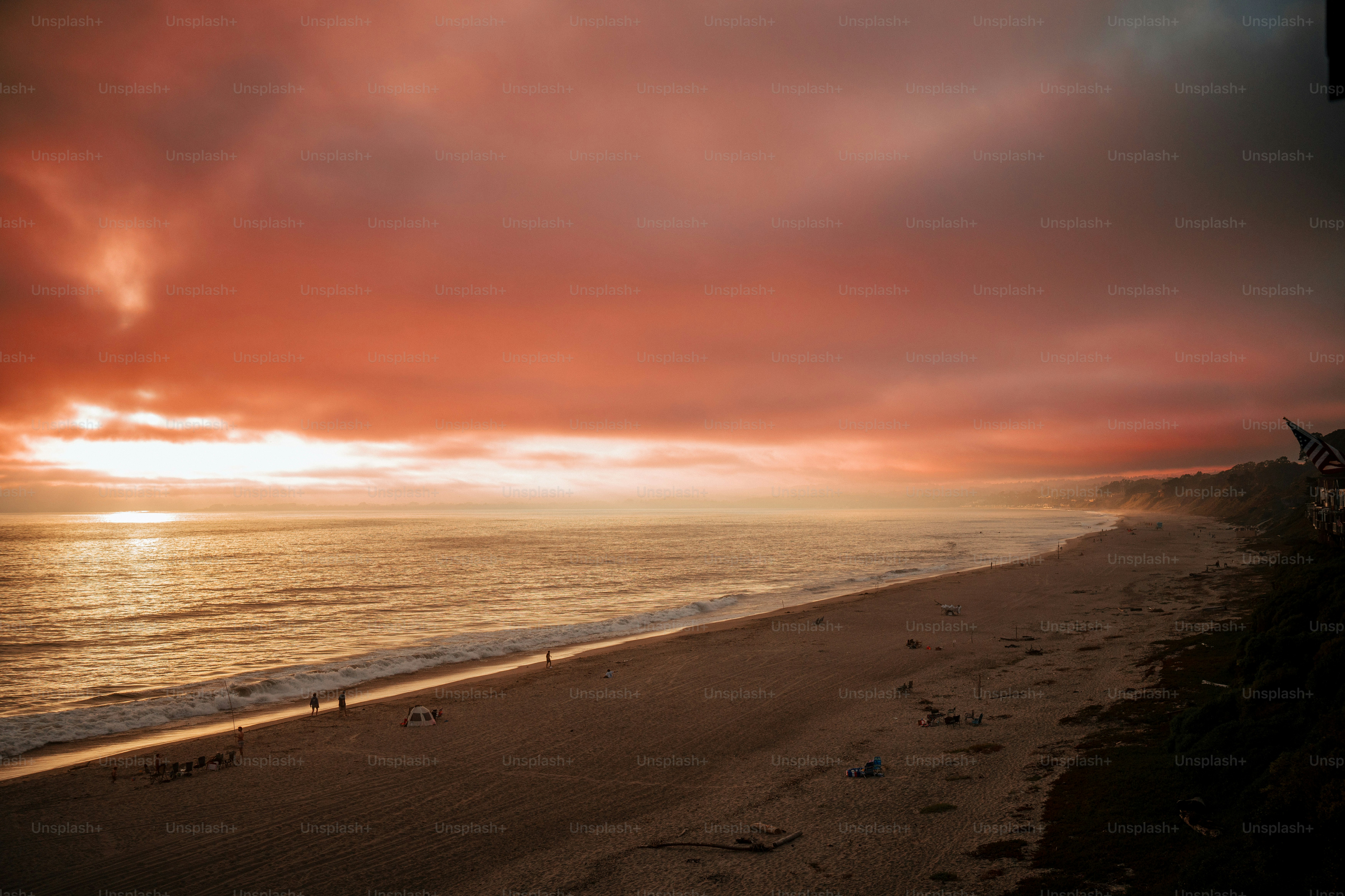 A sunset over a beach with a person walking on the beach