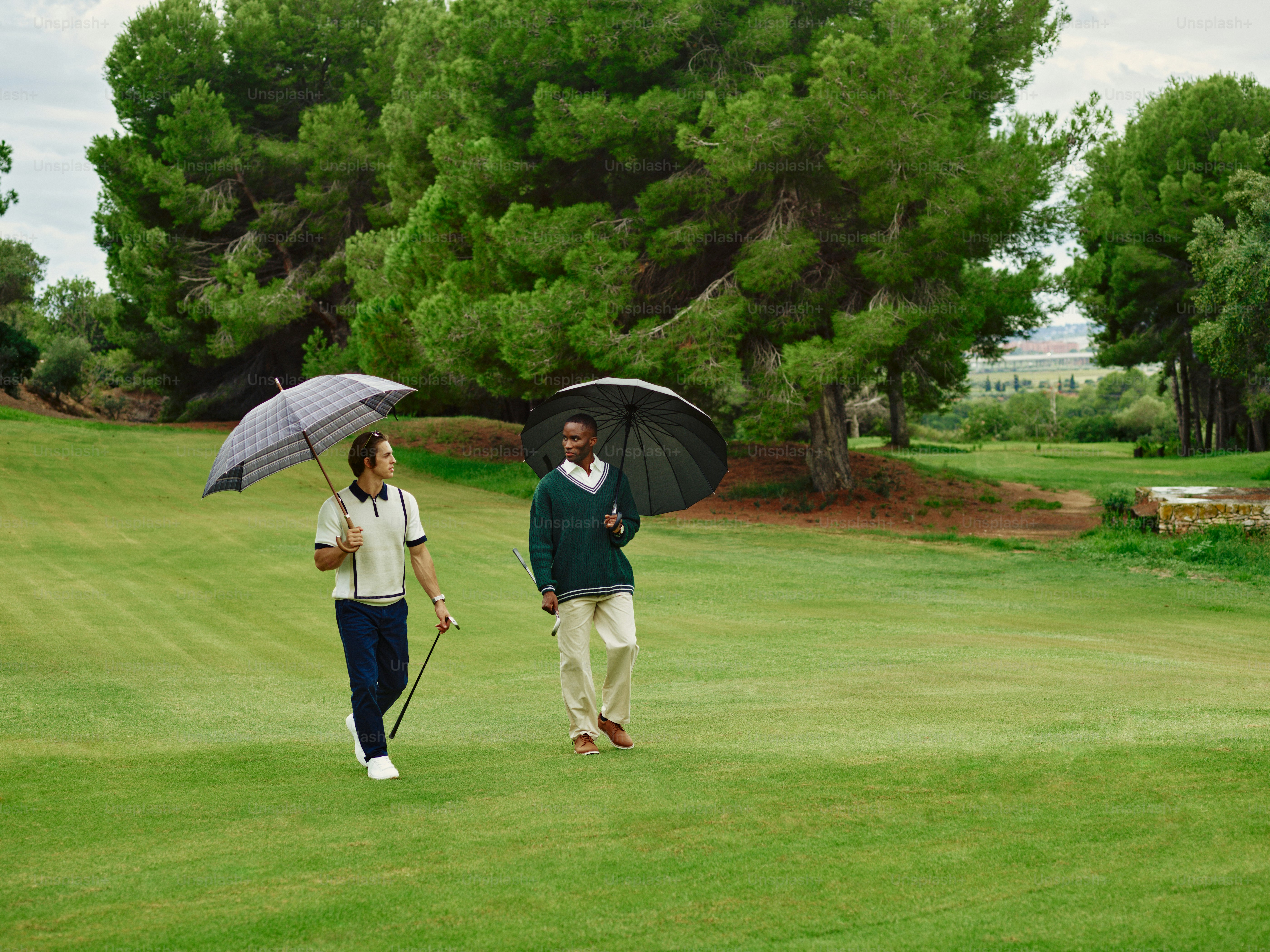 A couple of people walking across a field with umbrellas
