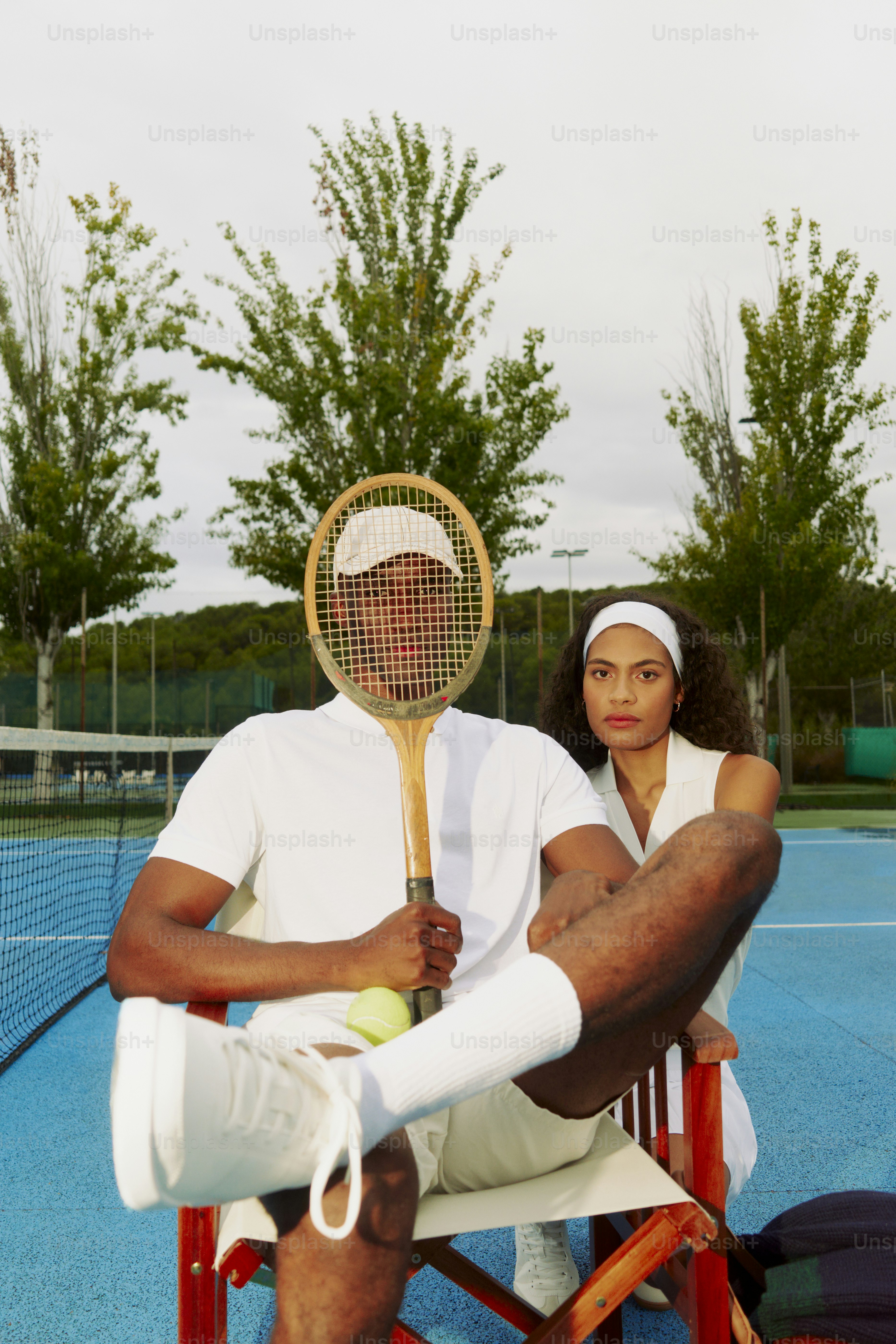 Seorang pria dan wanita duduk di kursi memegang raket tenis