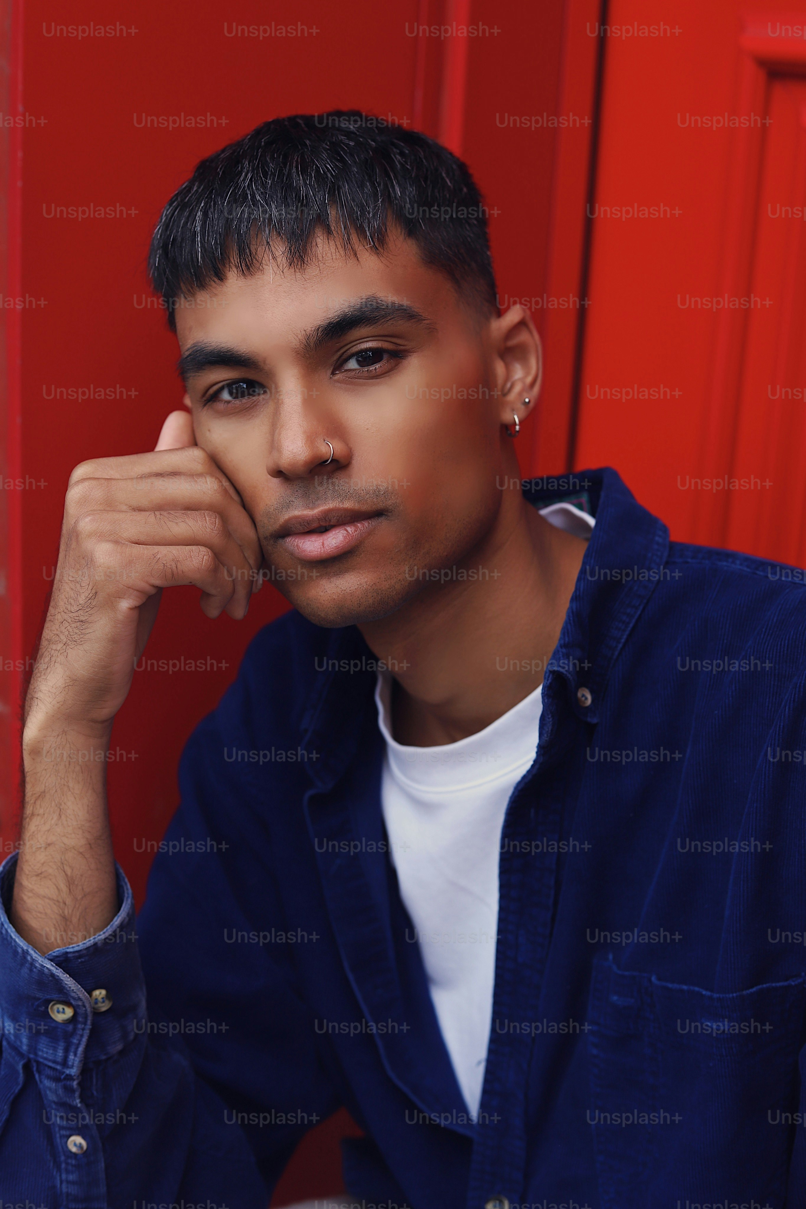 A young man sitting in front of a red door