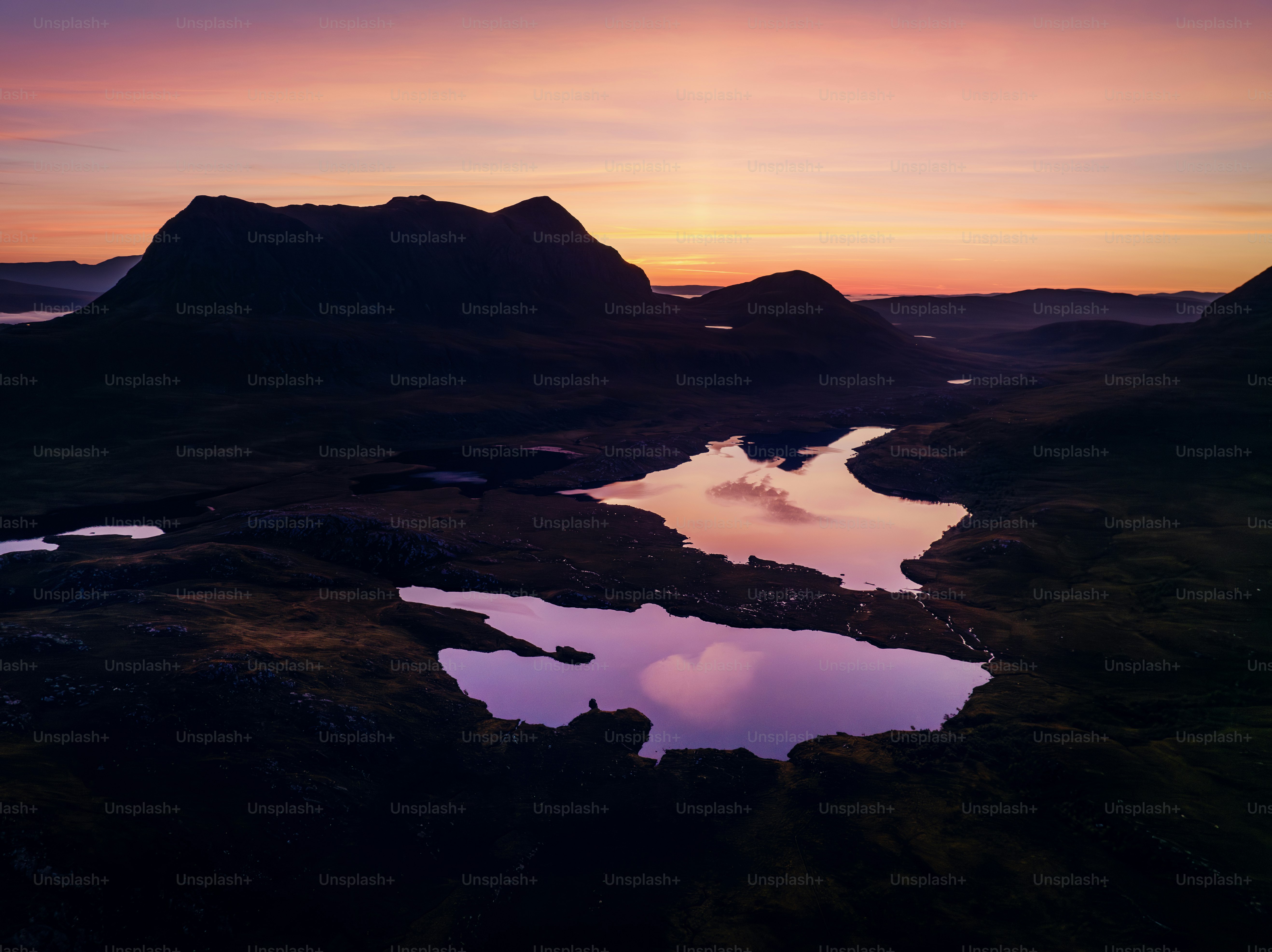 A sunset view of a mountain range with a lake in the foreground