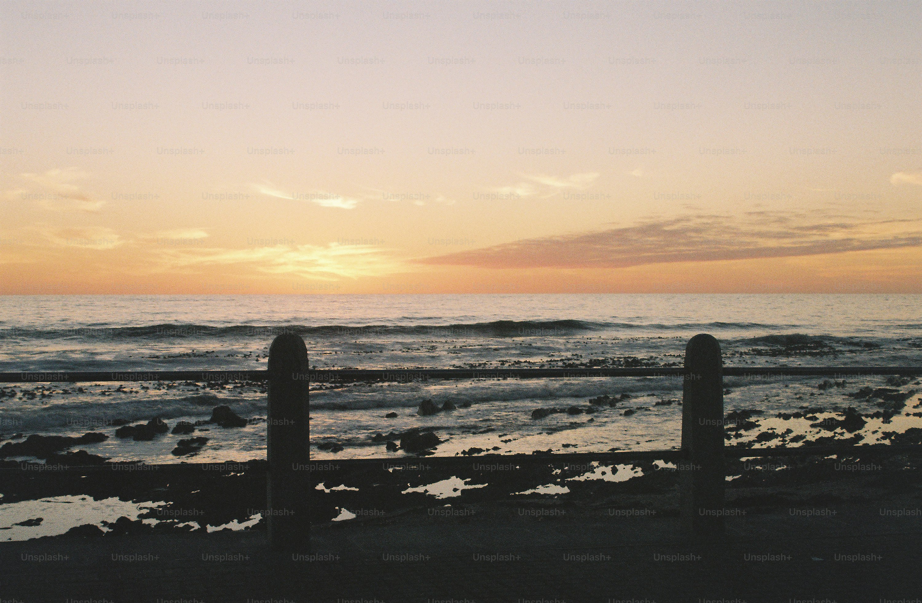 A sunset over the ocean with a fence in the foreground