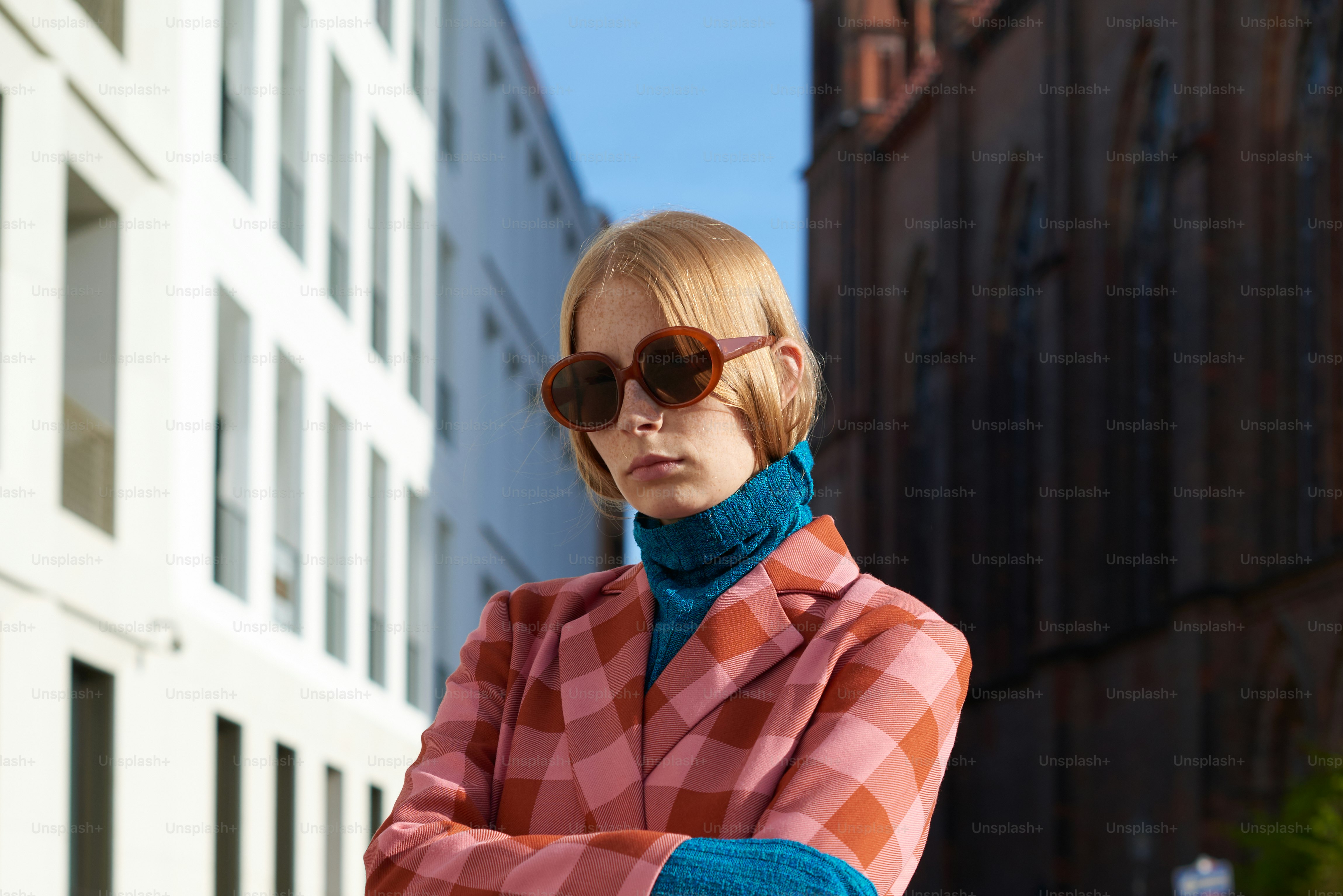 Una mujer con un abrigo a cuadros y gafas de sol apoyada en un edificio