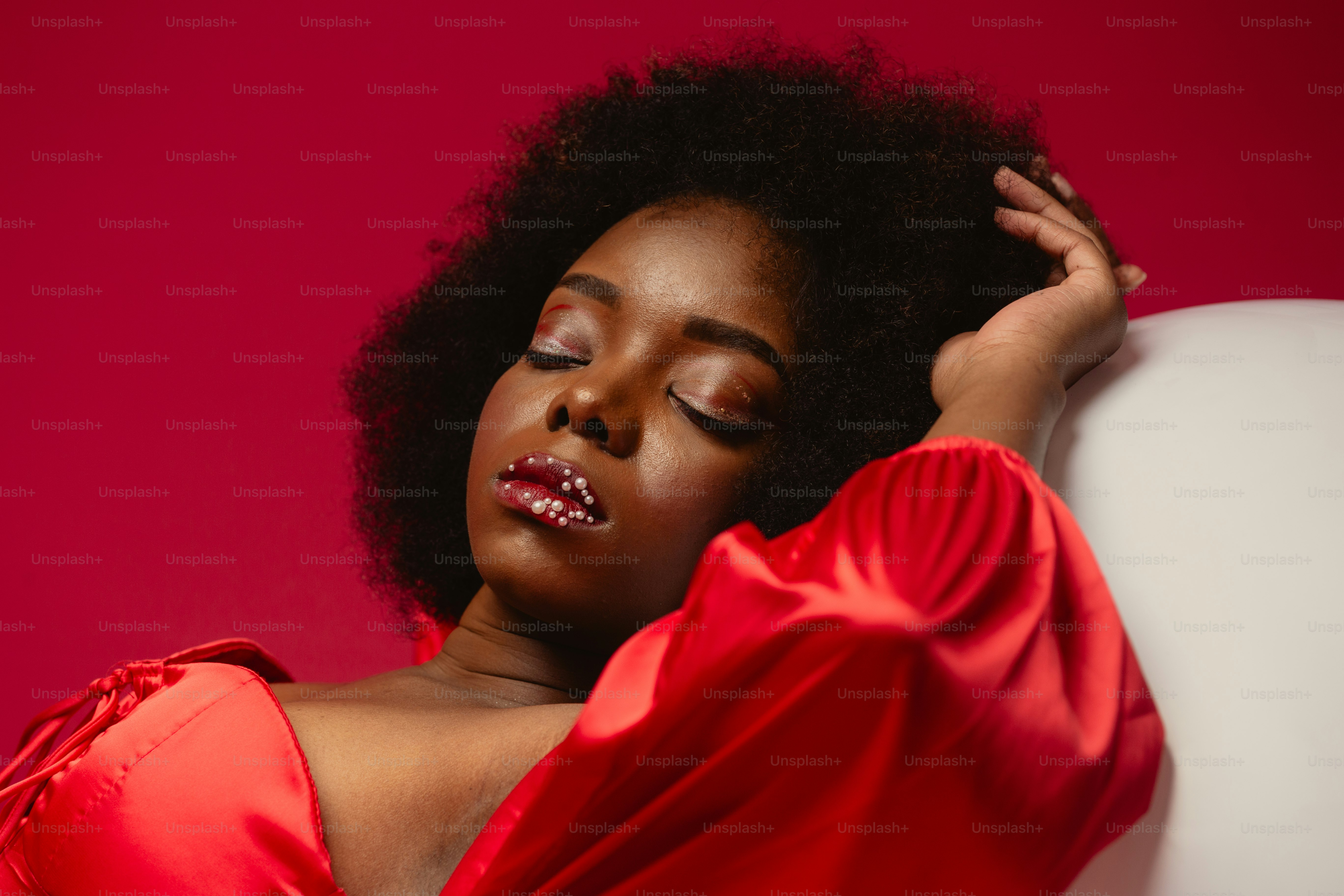 Una donna in un vestito rosso appoggiata a un muro bianco