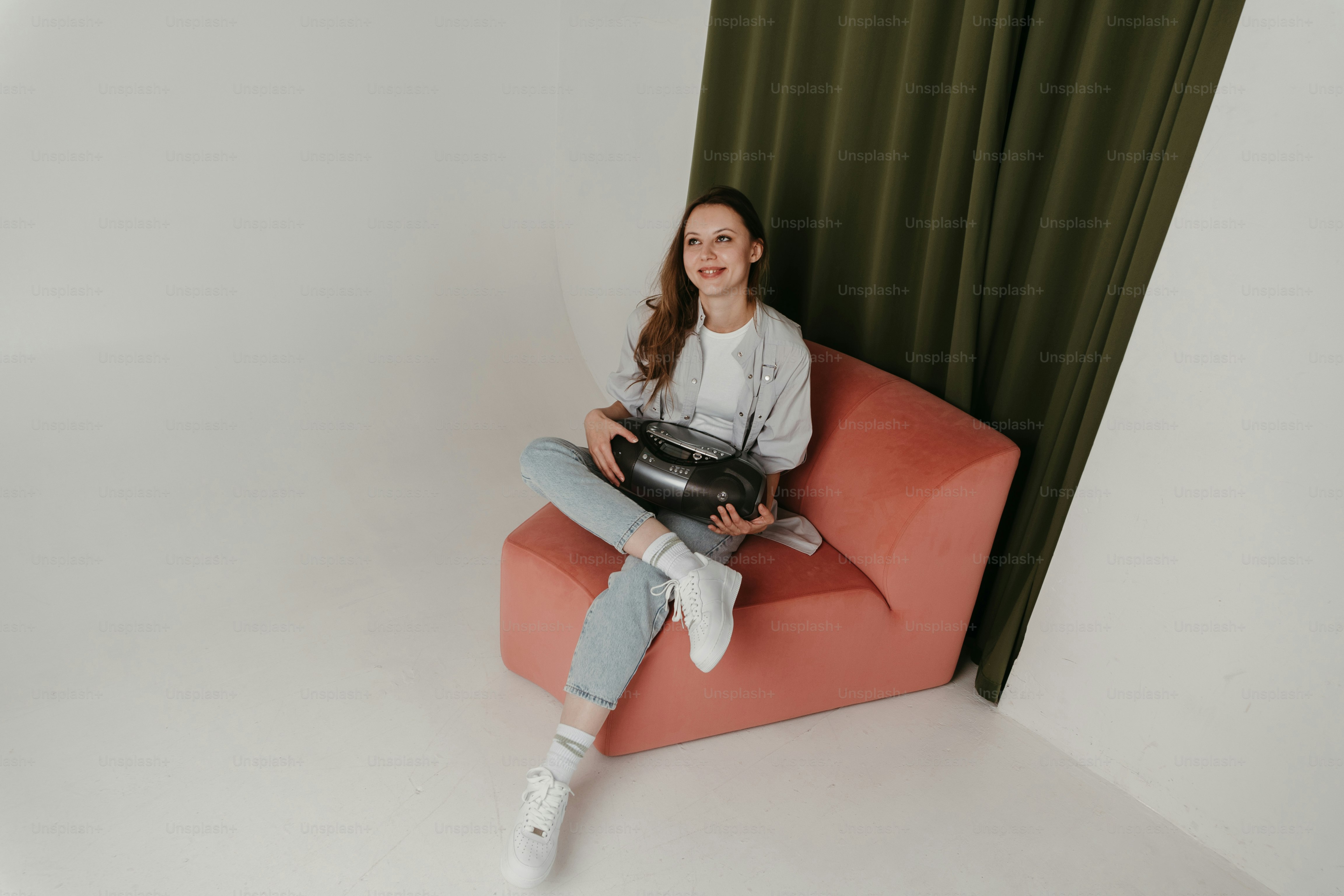 緑のカーテンの前で赤い椅子に座る女性