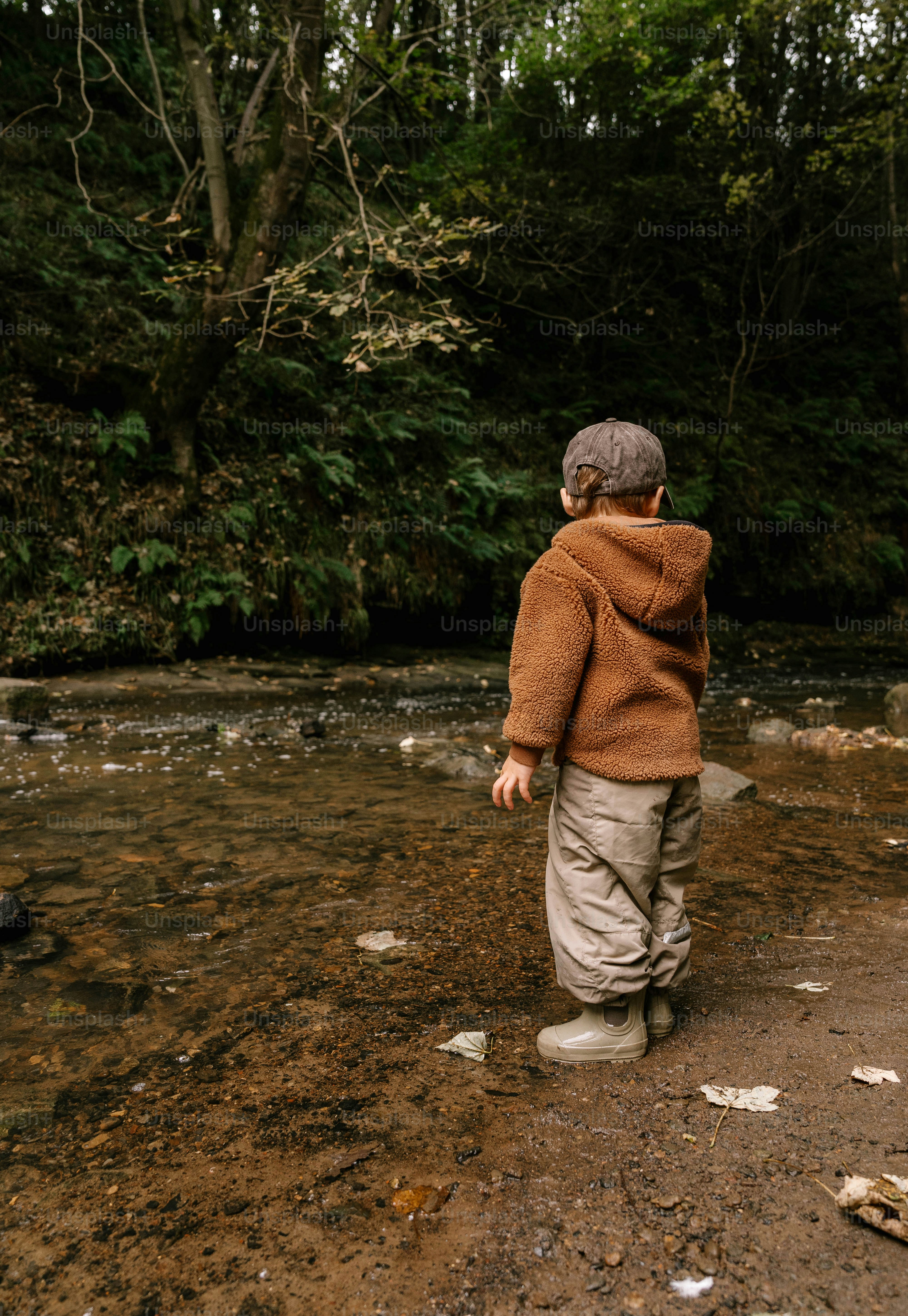 Ein kleiner Junge geht über einen Fluss neben einem Wald