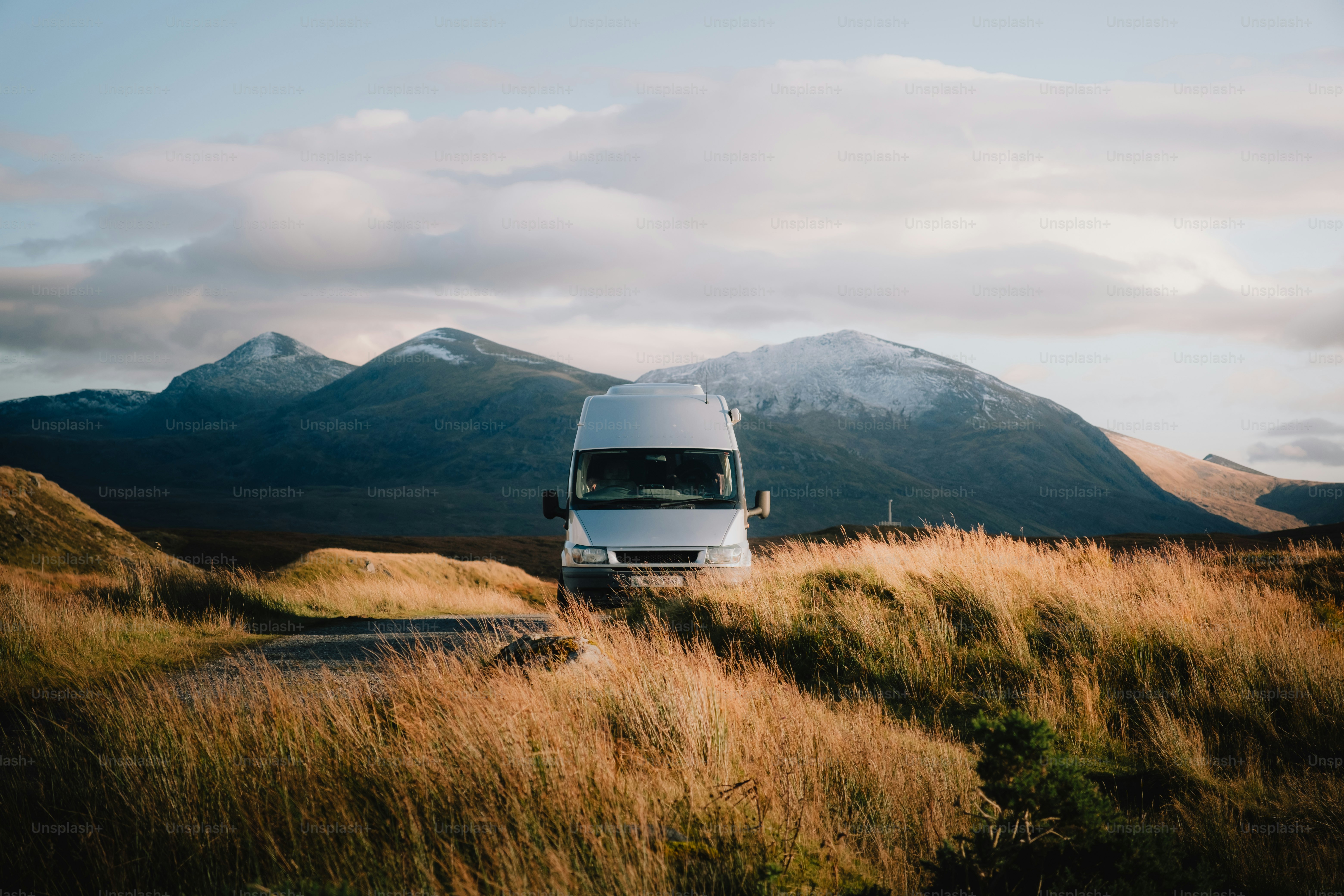 A van is parked in a field with mountains in the background