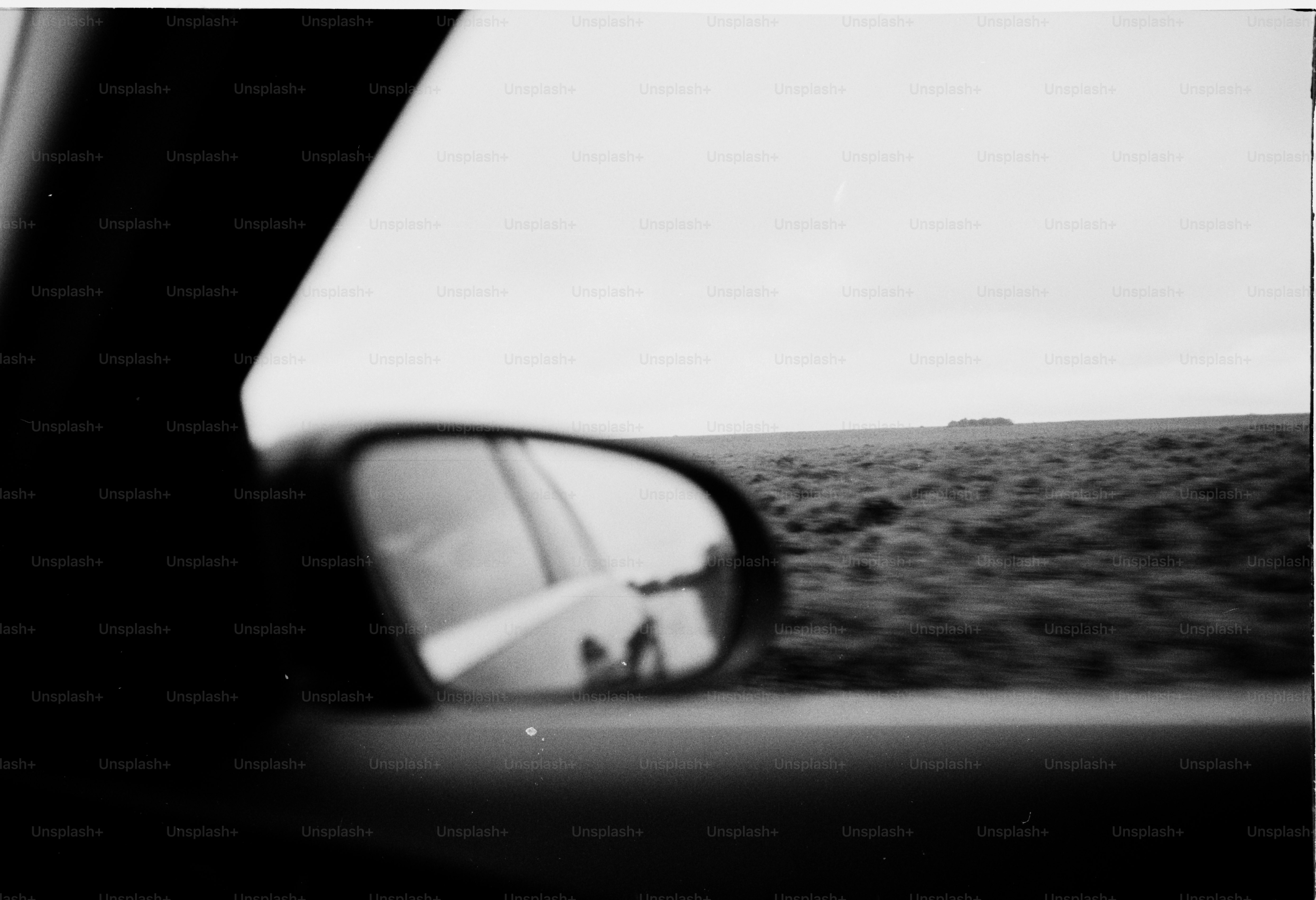 A car's side view mirror is shown in a black and white photo