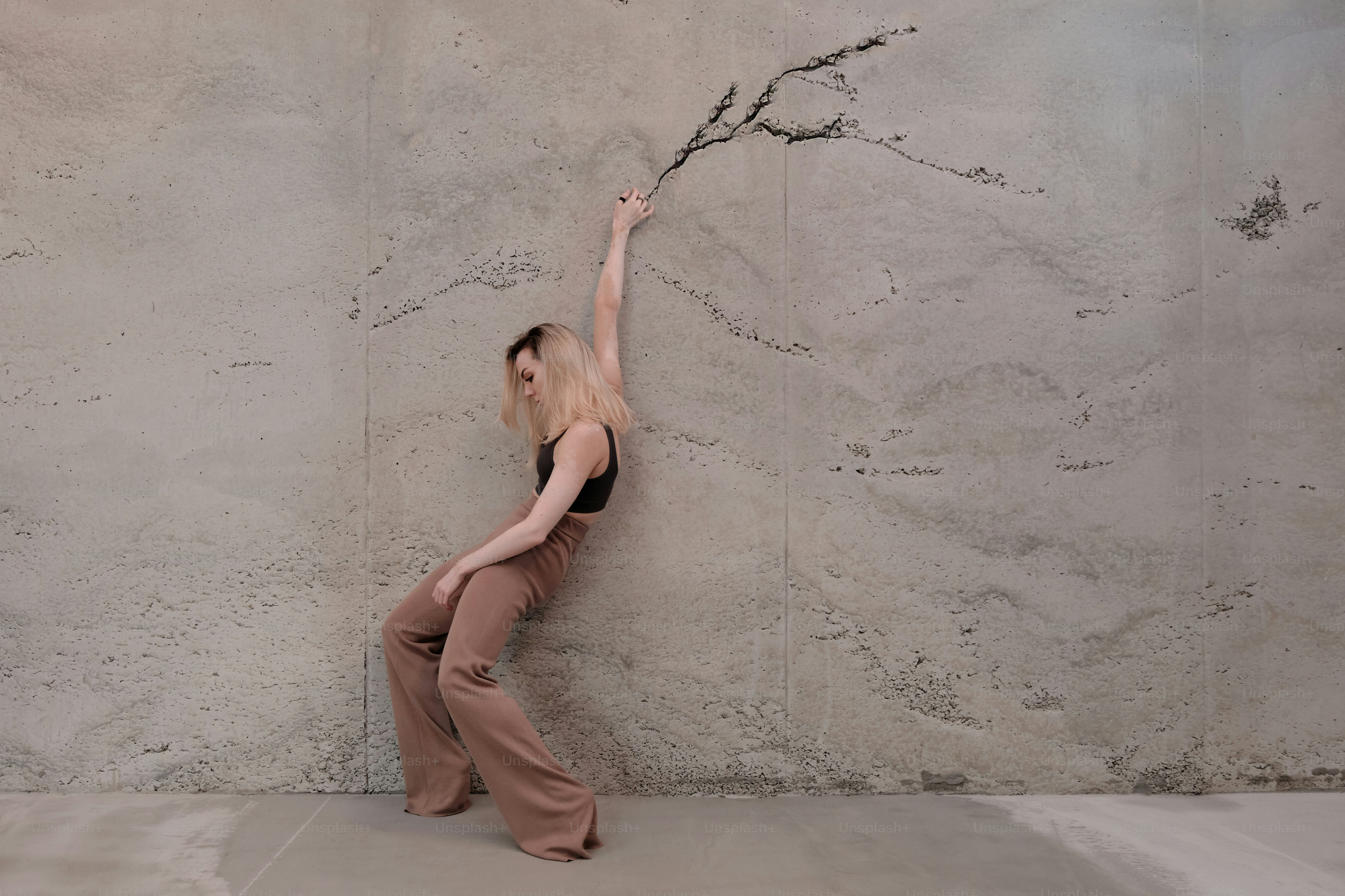 A woman standing in front of a wall holding a branch