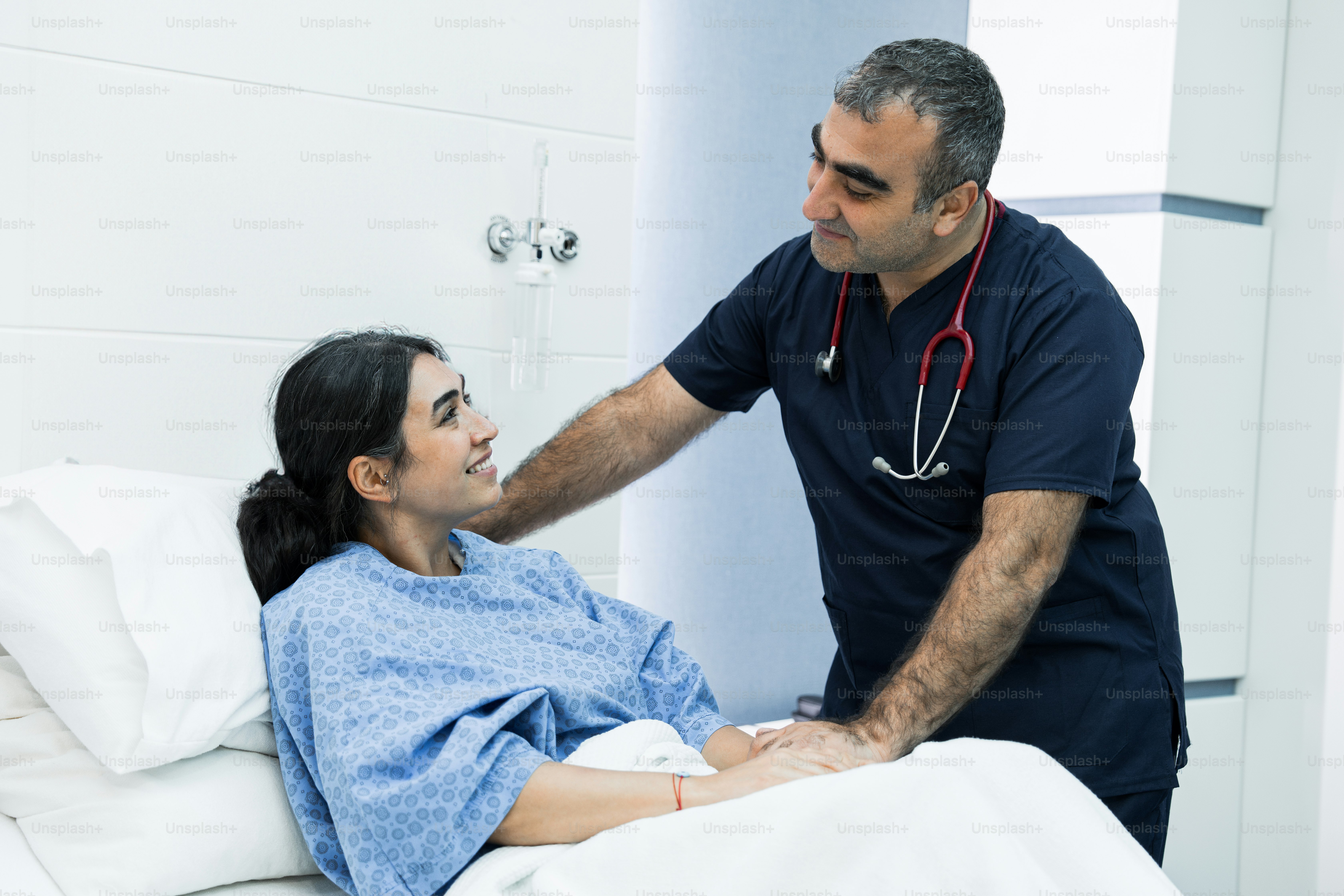 A man in a blue shirt is talking to a woman in a hospital bed
