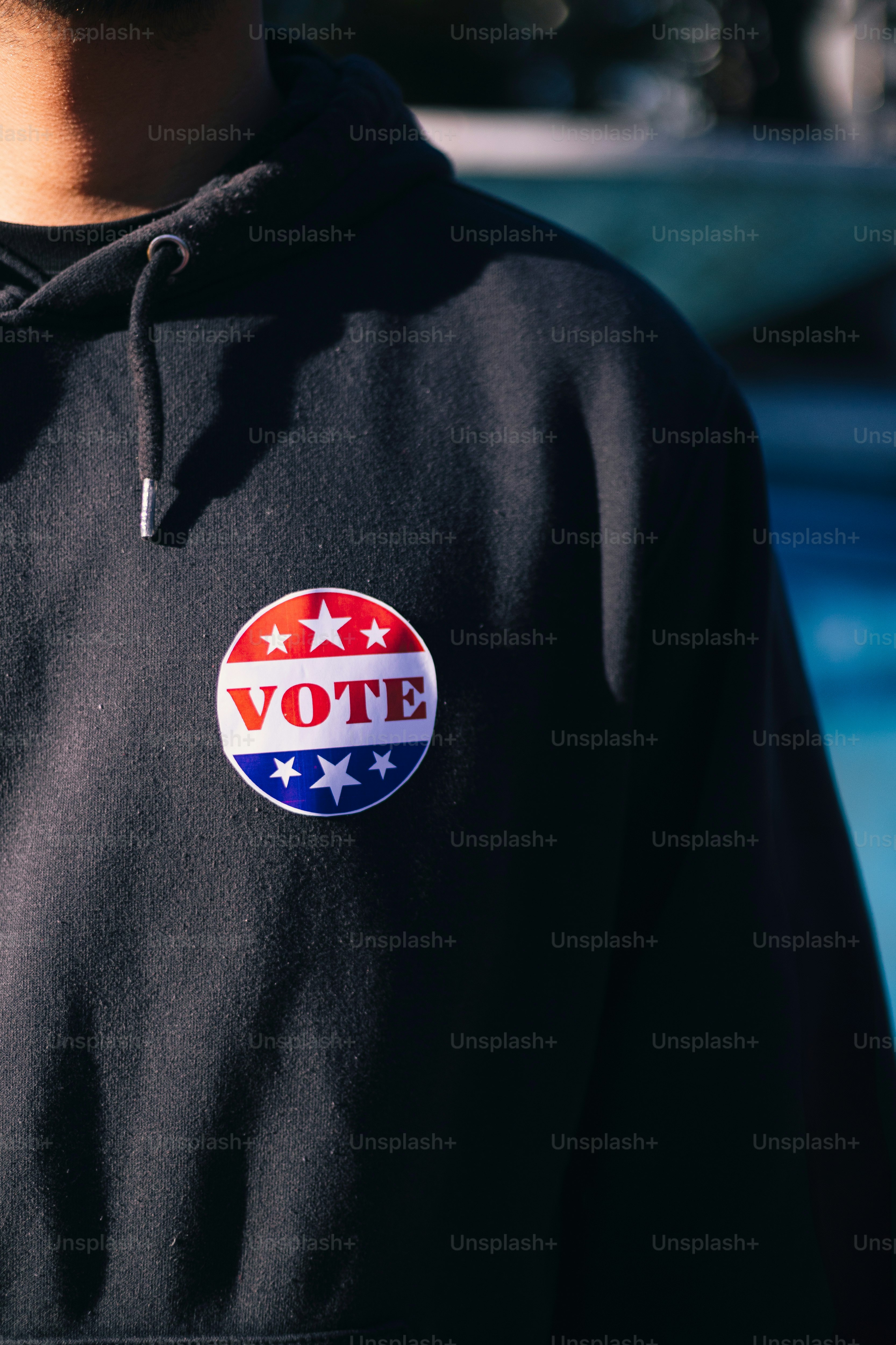 A man in a black hoodie with a vote sticker on it