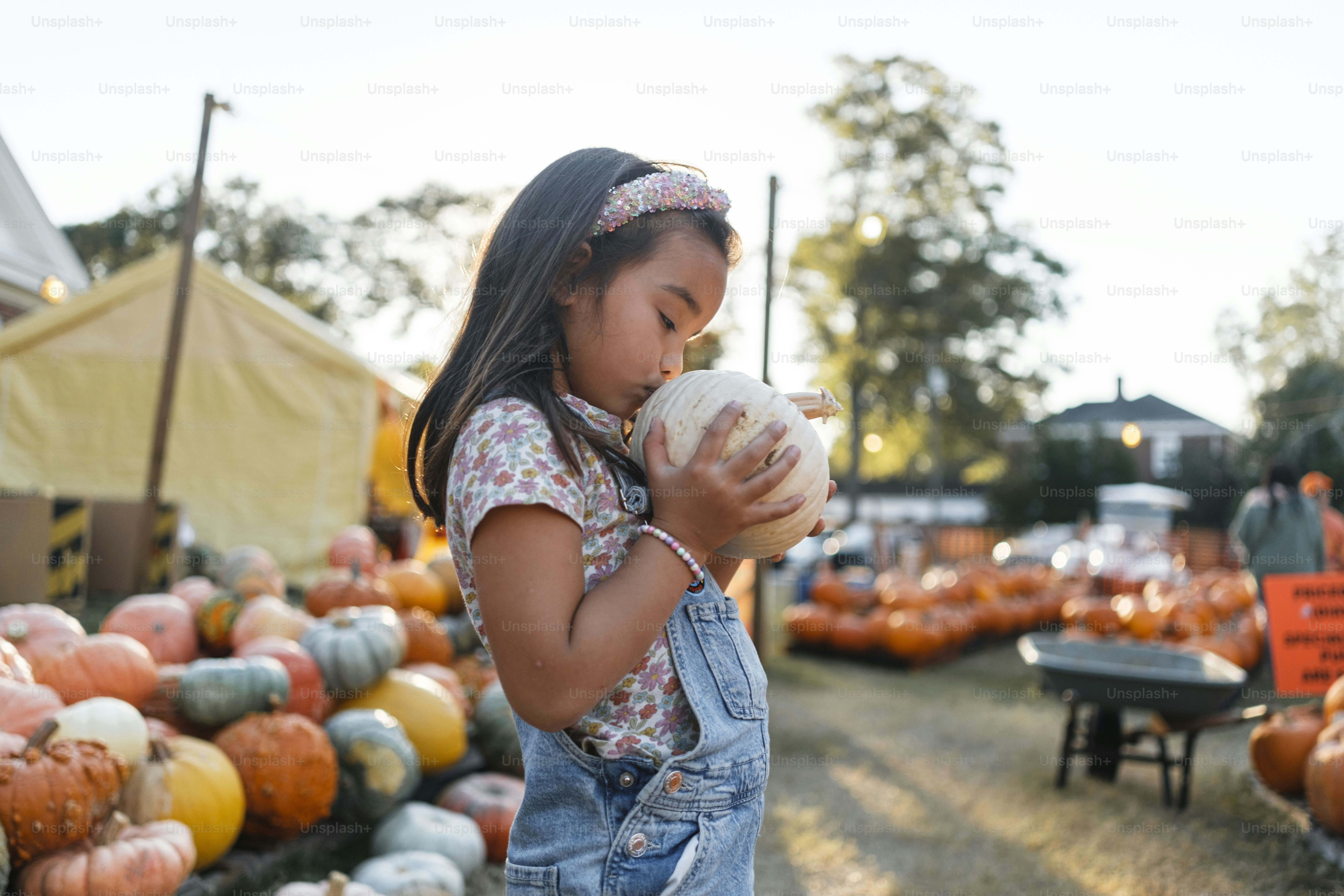 A little girl standing in front of a pile of pumpkins photo – Girl ...