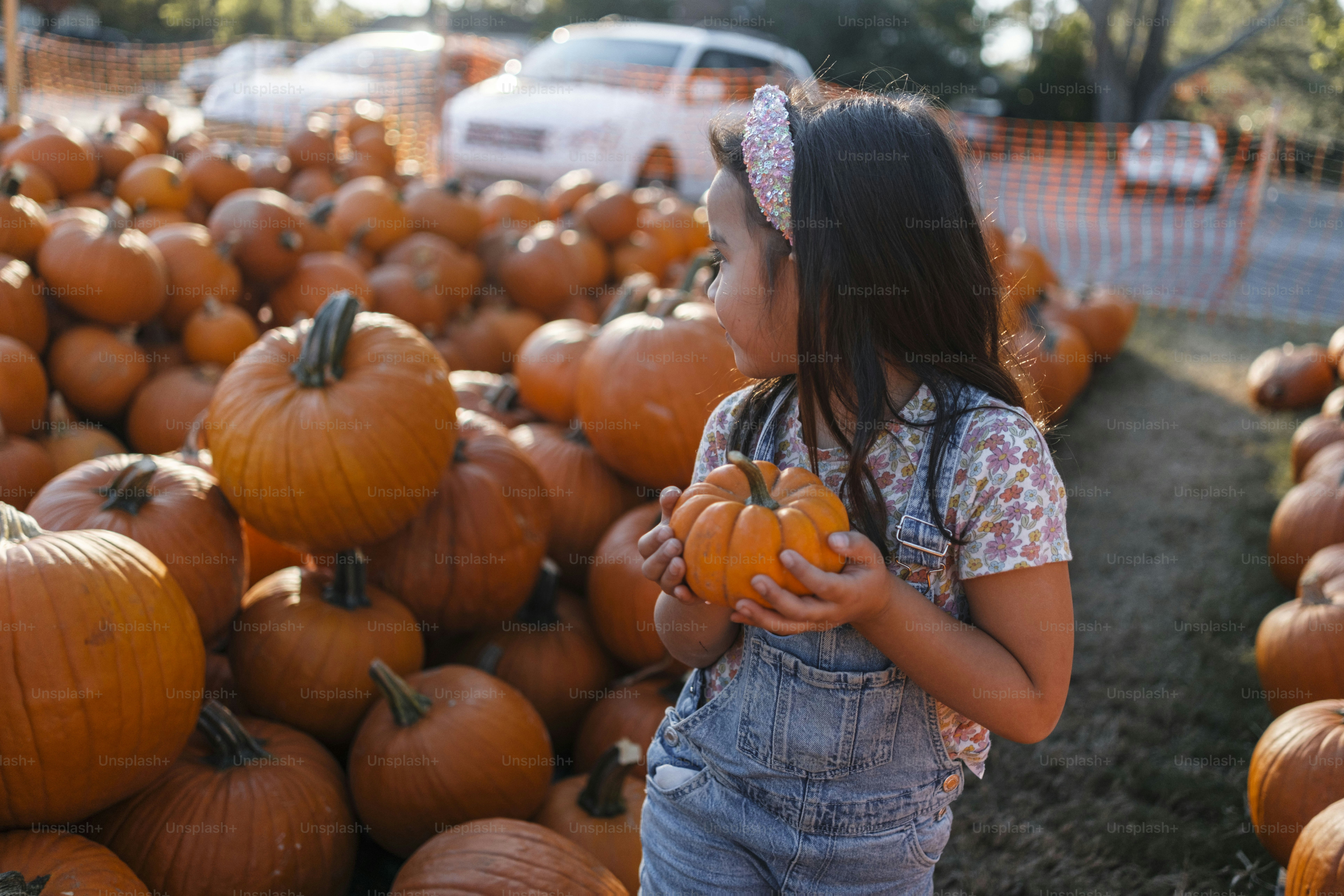 A little girl standing next to a pile of pumpkins