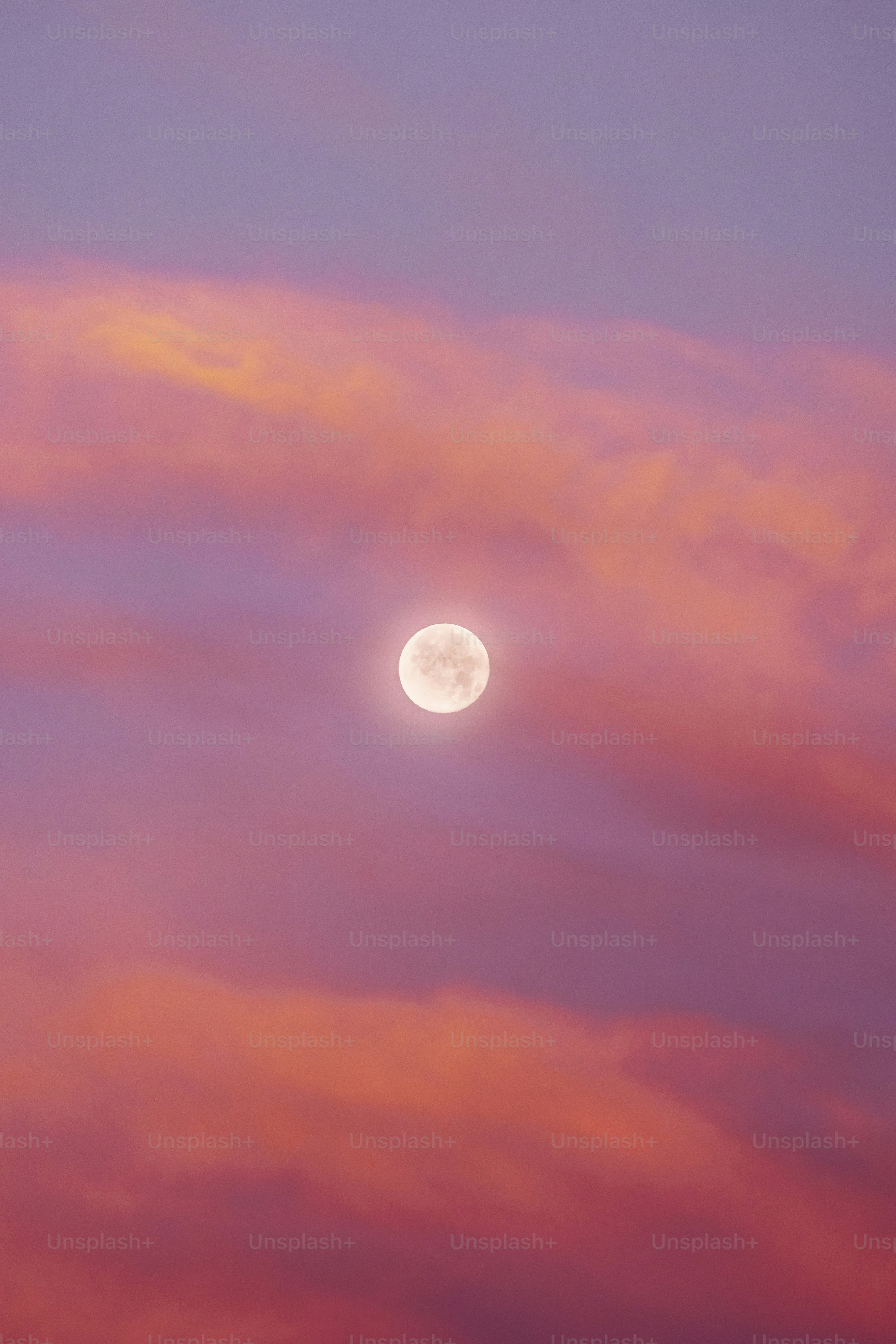 A full moon in a pink sky with clouds