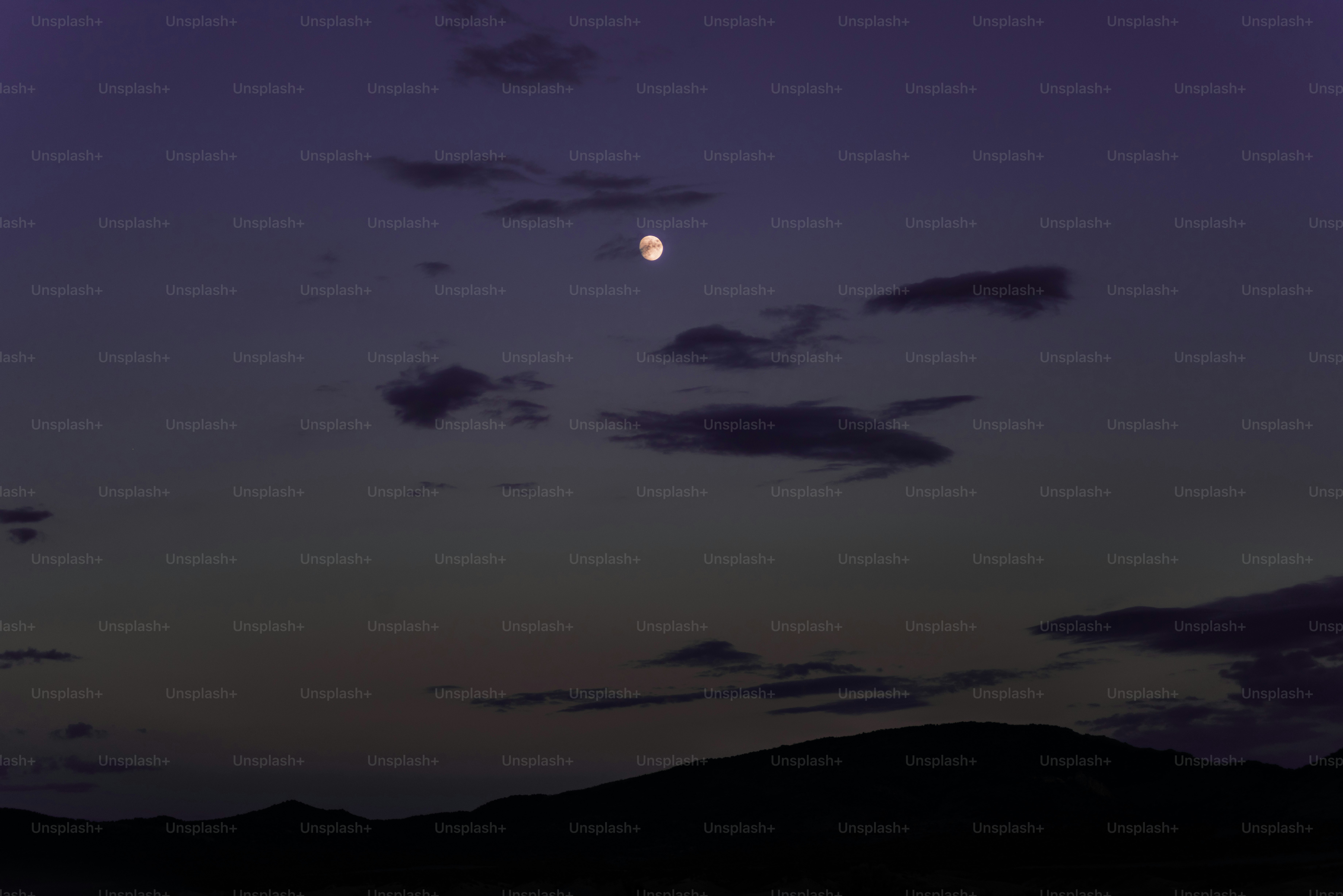 Una luna piena è visibile nel cielo sopra una catena montuosa